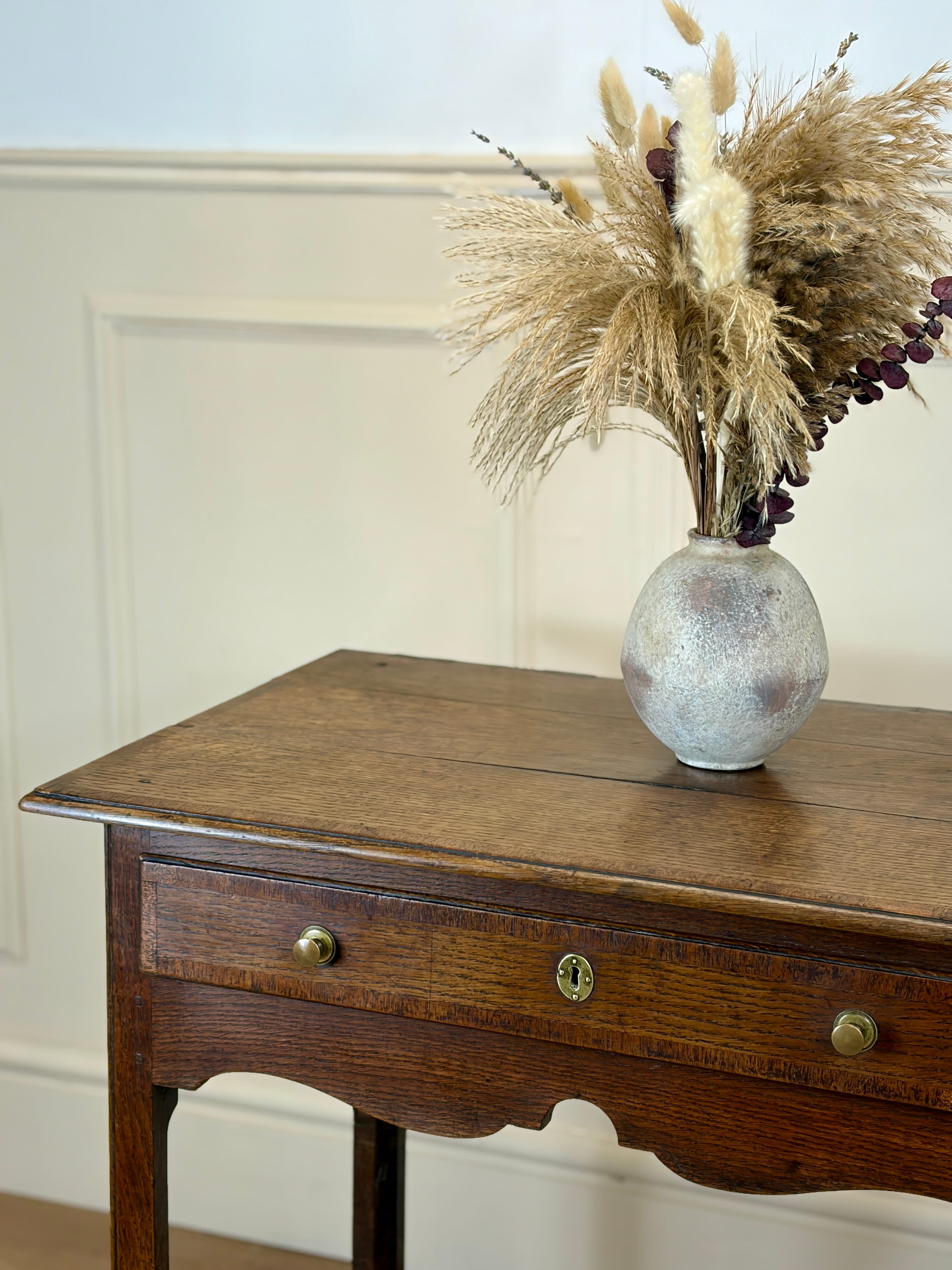 Wooden side table with a vase of dried plants on a neutral background