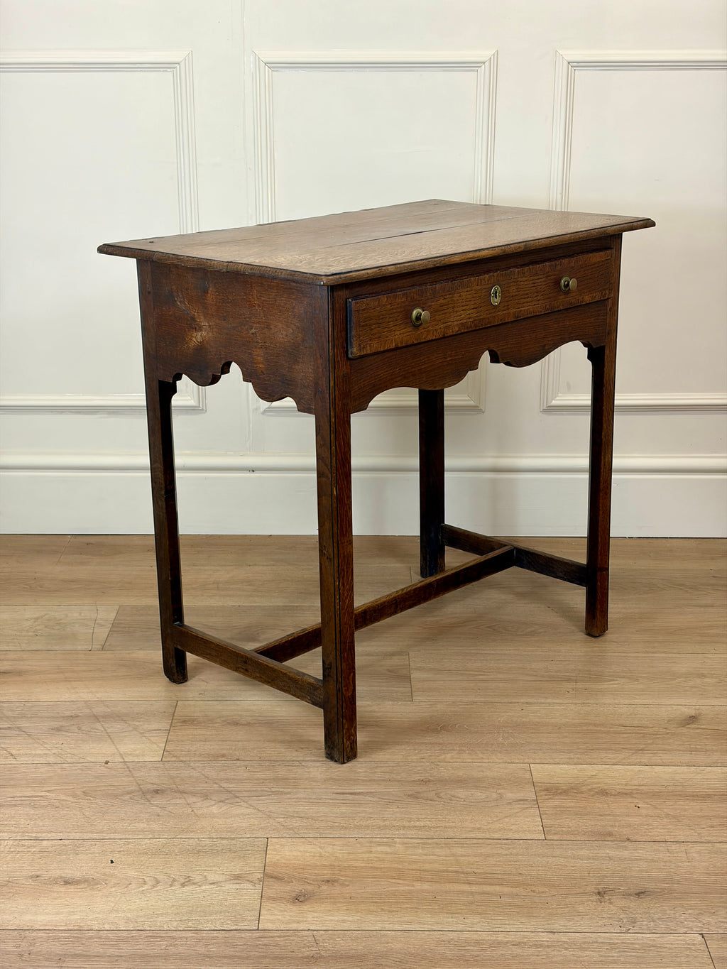 Wooden side table with a single drawer on a wooden floor.