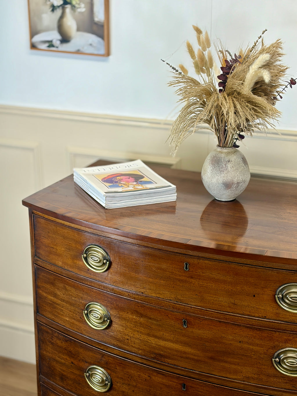 Wooden dresser with a vase of dried plants and a stack of books on top.