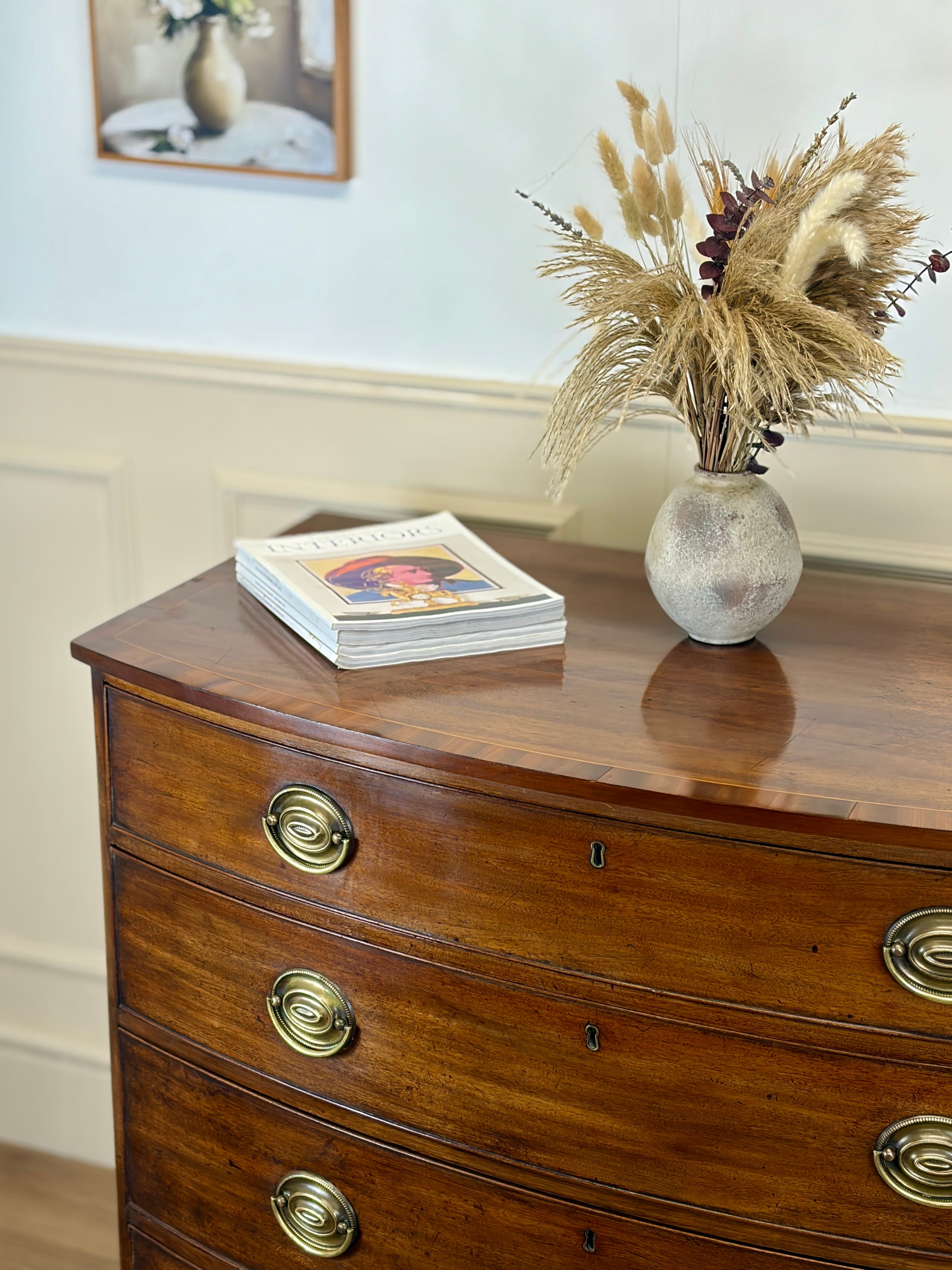 Wooden dresser with a vase of dried plants and a stack of books on top.