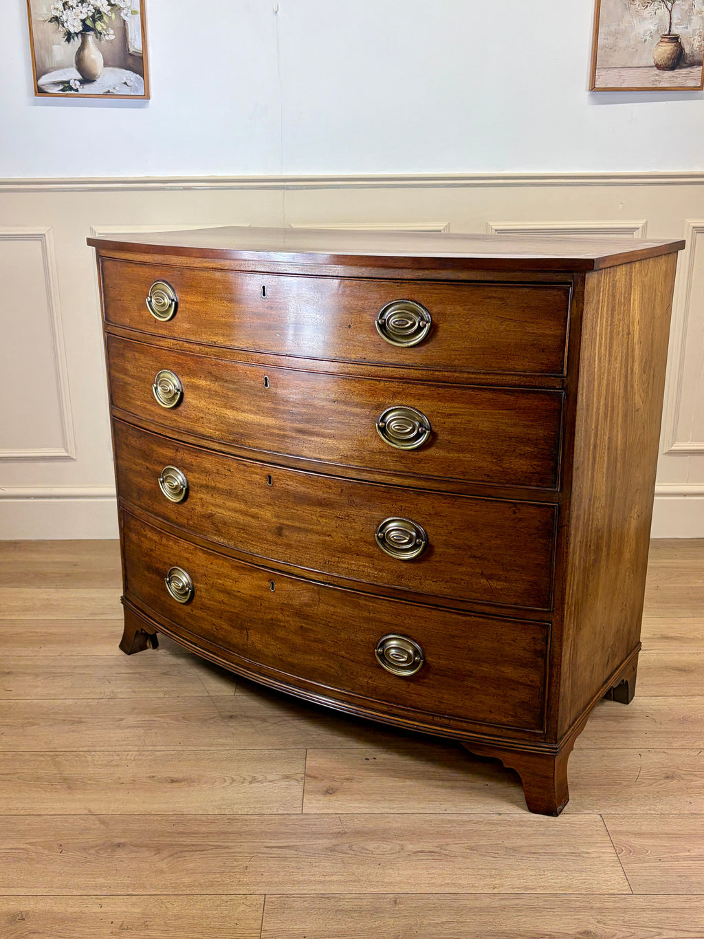 Wooden dresser with curved design and metal handles on a wooden floor.