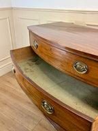 Wooden sideboard with curved design and brass handles in a room with wainscoting.