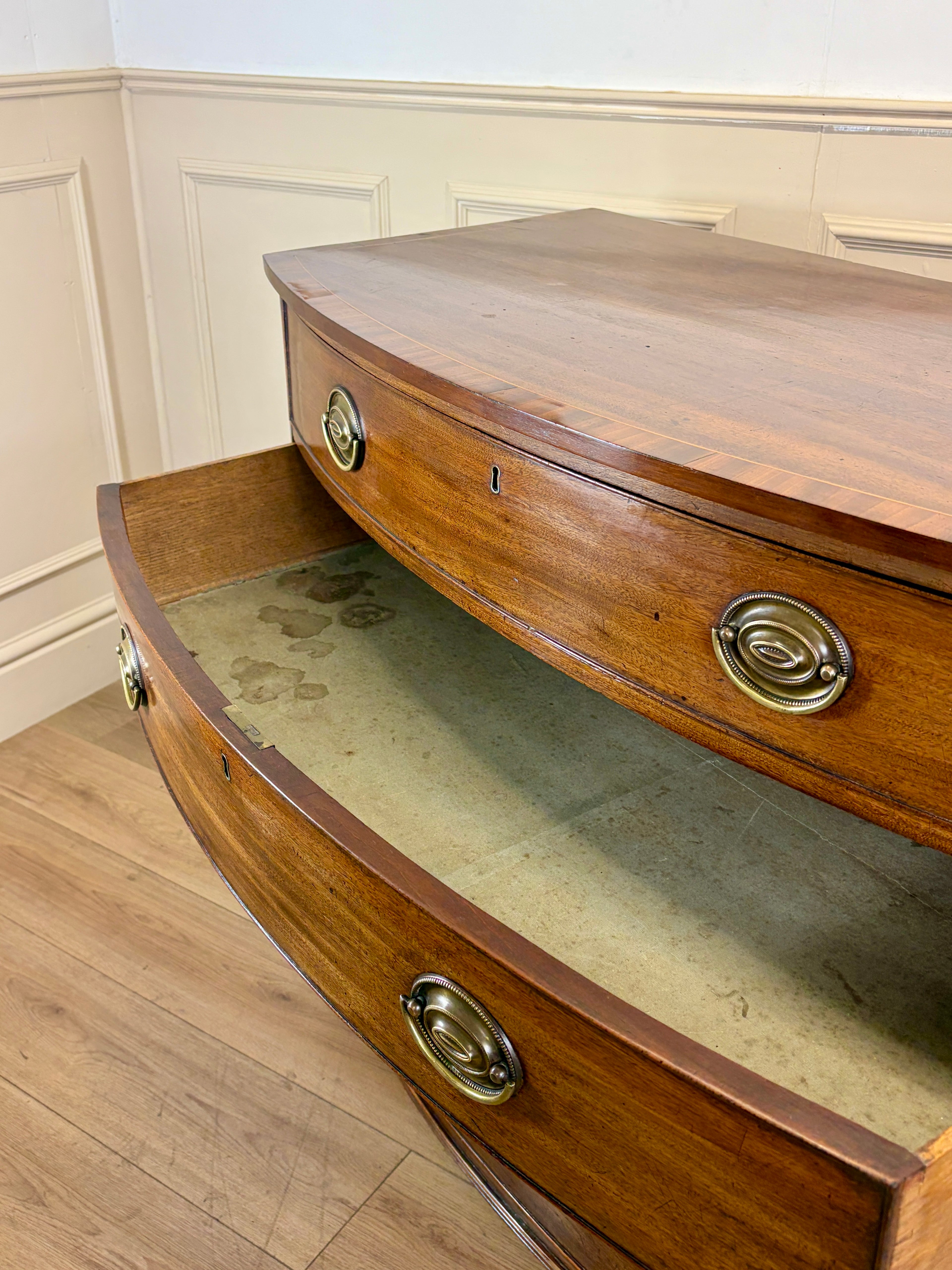 Wooden sideboard with curved design and brass handles in a room with wainscoting.