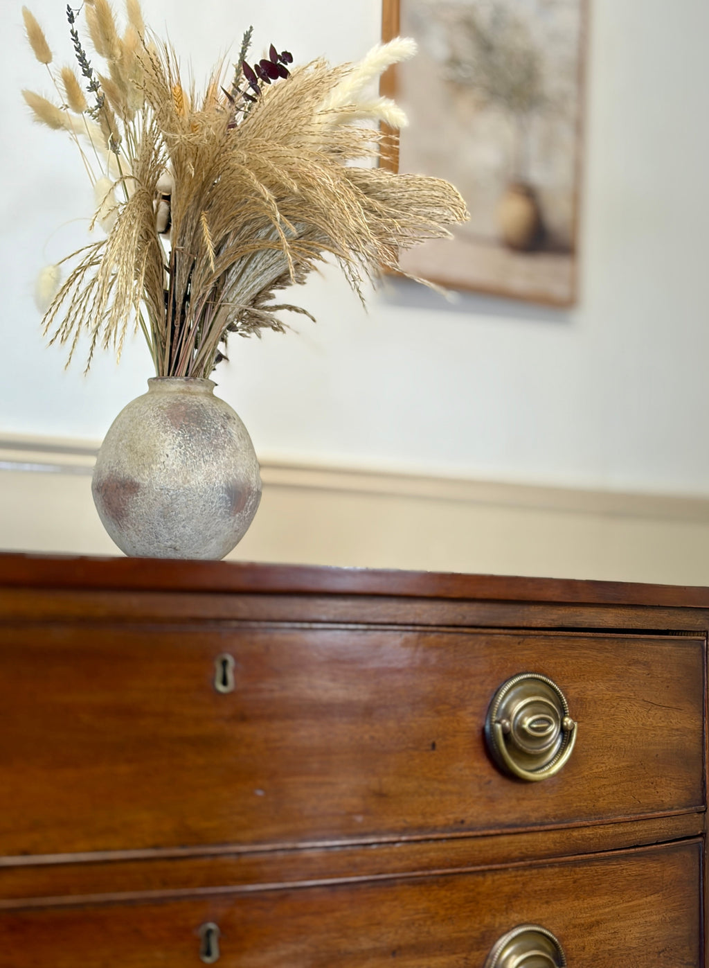 Decorative vase with dried plants on a wooden dresser
