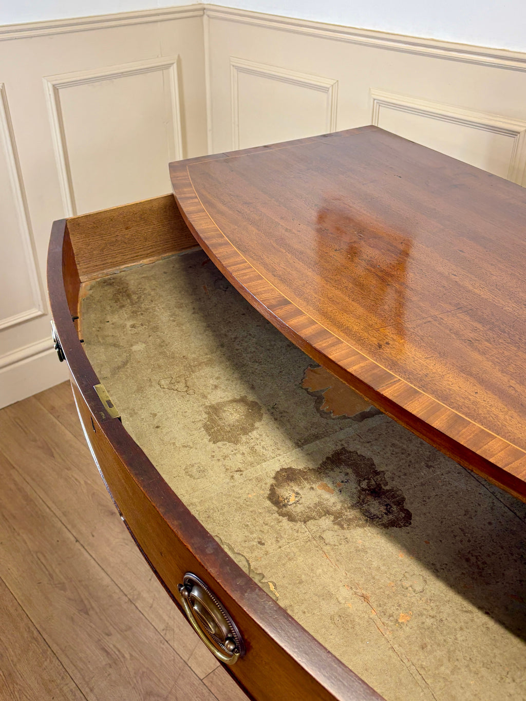 Wooden desk with glass top in a room with white paneled walls.