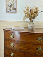 Wooden dresser with brass handles featuring a vase of dried plants and books on top.