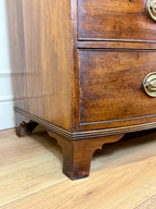 Close-up of a wooden dresser with brass handles on a wooden floor.