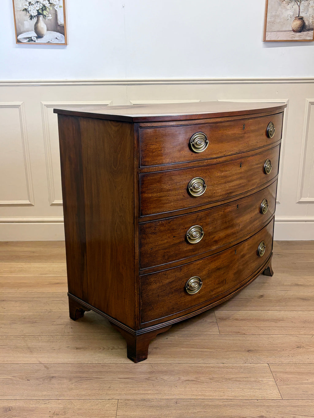 Wooden bowfront chest of drawers with brass handles on a wooden floor.
