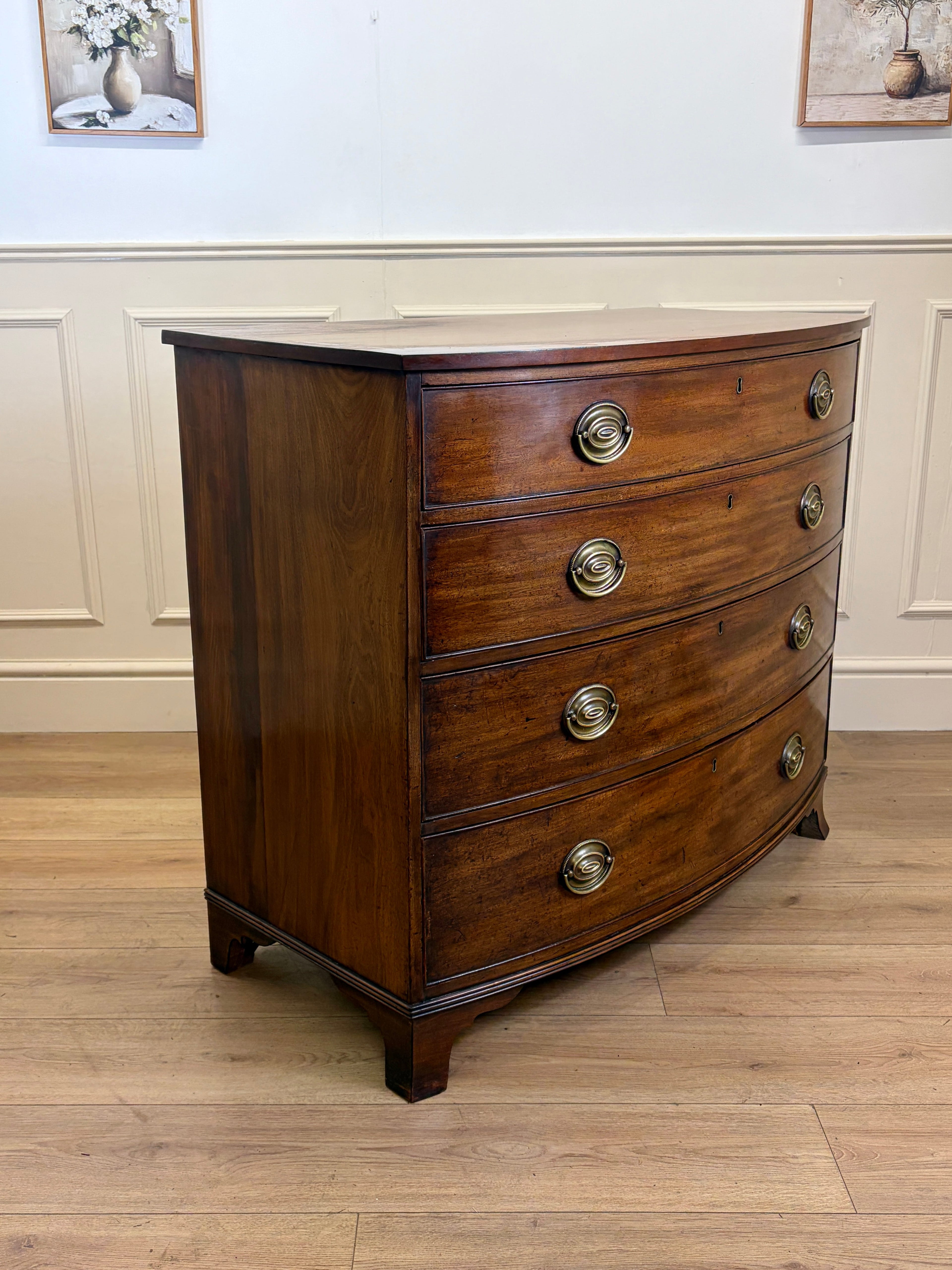 Wooden bowfront chest of drawers with brass handles on a wooden floor.