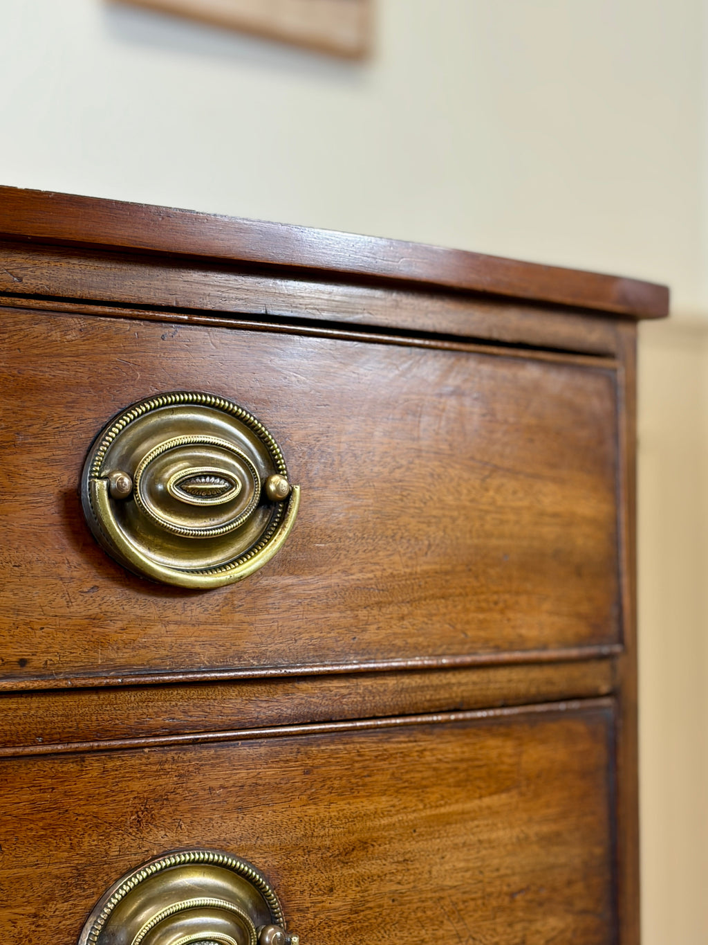 Close-up of a wooden drawer with brass handles on a beige wall background