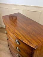Wooden dresser with curved top and drawers against a white paneled wall.