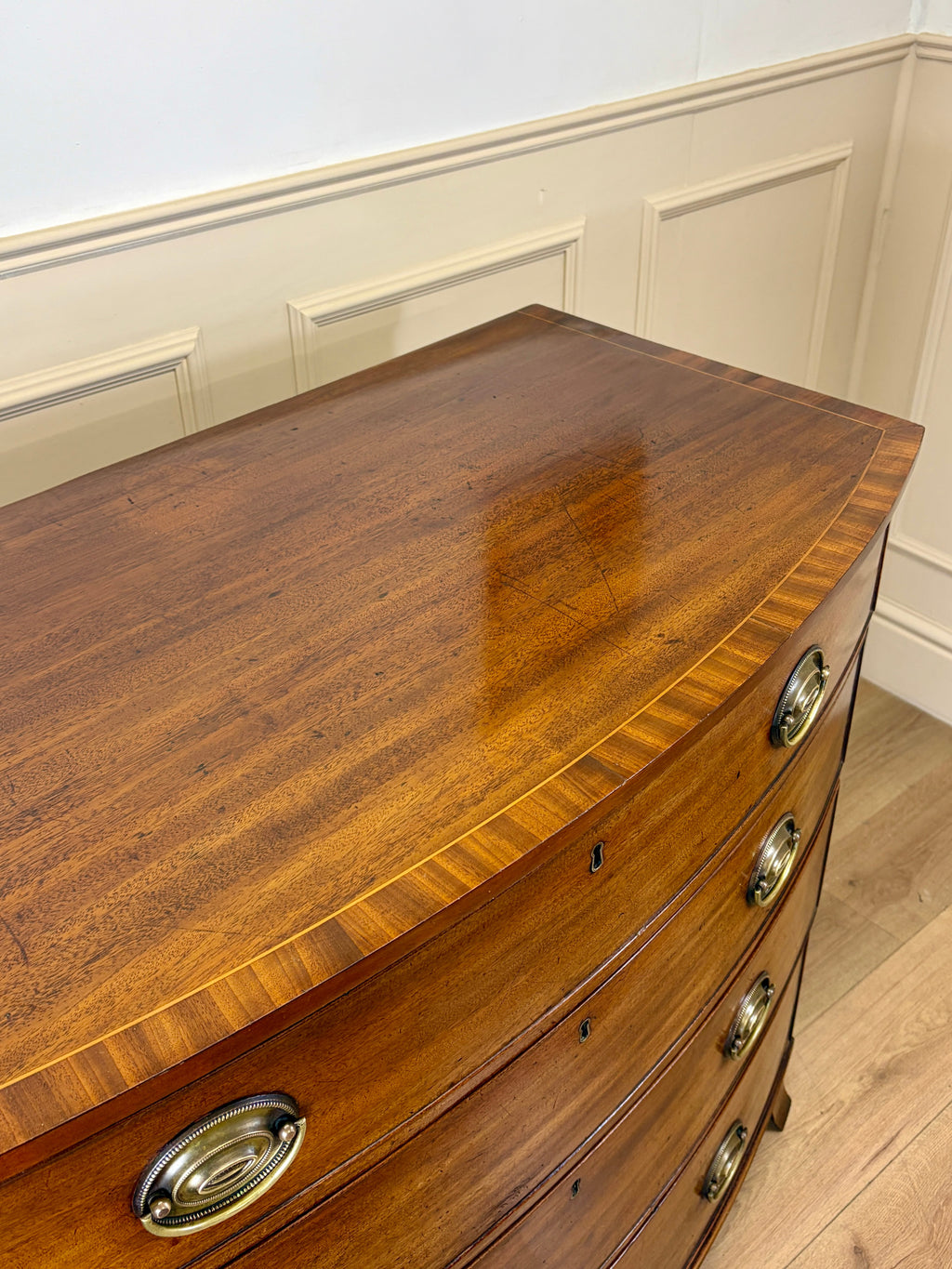 Wooden dresser with curved top and brass handles in a room with white walls and wooden floor.