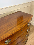 Wooden dresser with curved top and brass handles in a room with white walls and wooden floor.