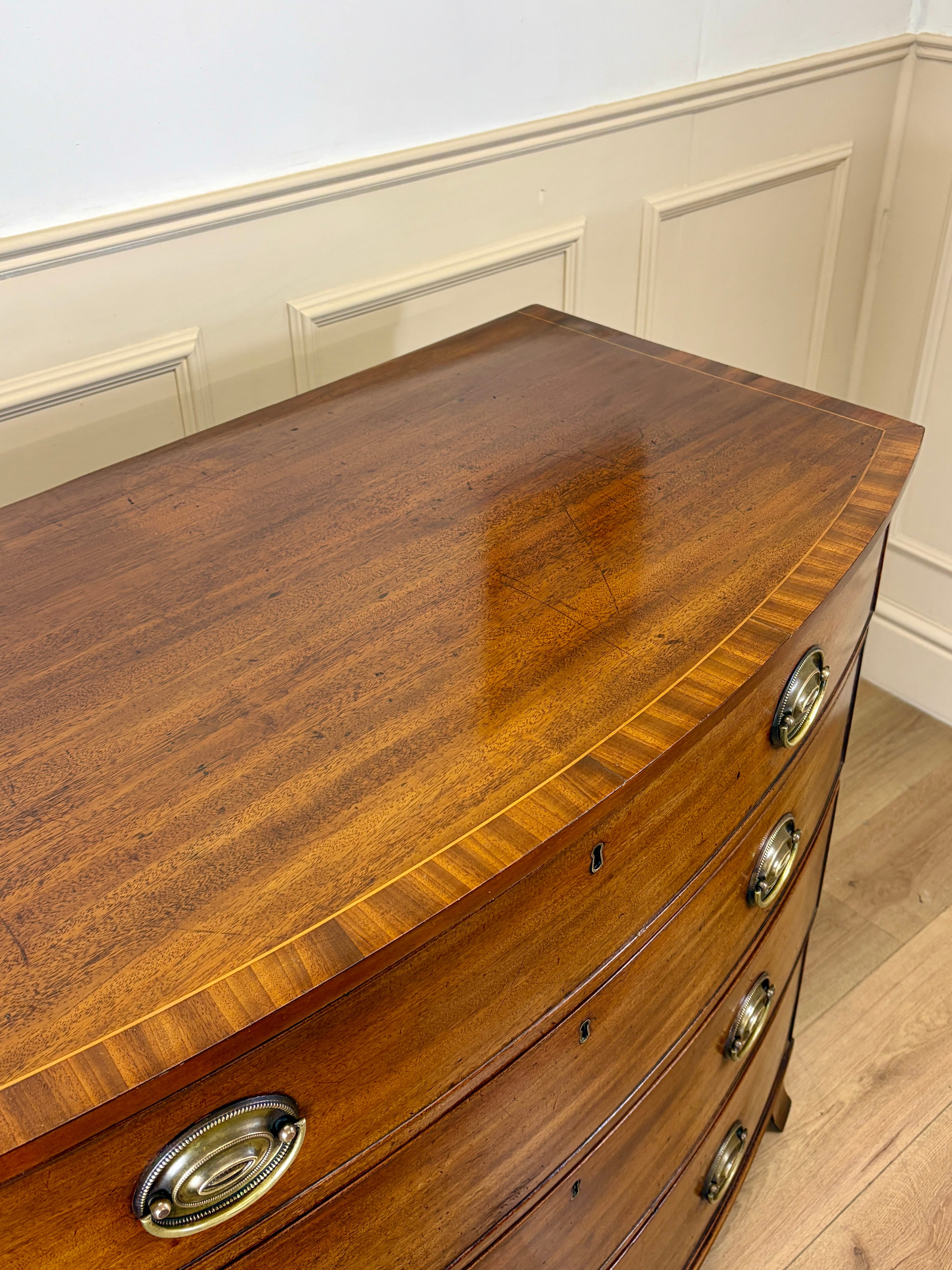 Wooden dresser with curved top and brass handles in a room with white walls and wooden floor.