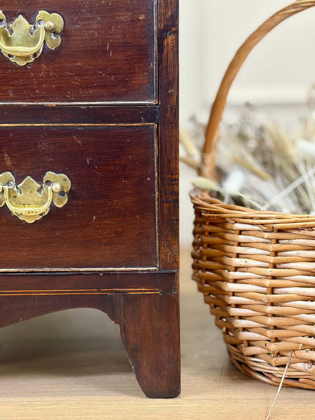 Wooden drawer with brass handles next to a wicker basket on a wooden surface.
