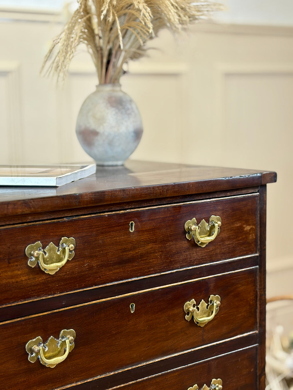 Wooden dresser with brass handles and a vase on top against a neutral wall.