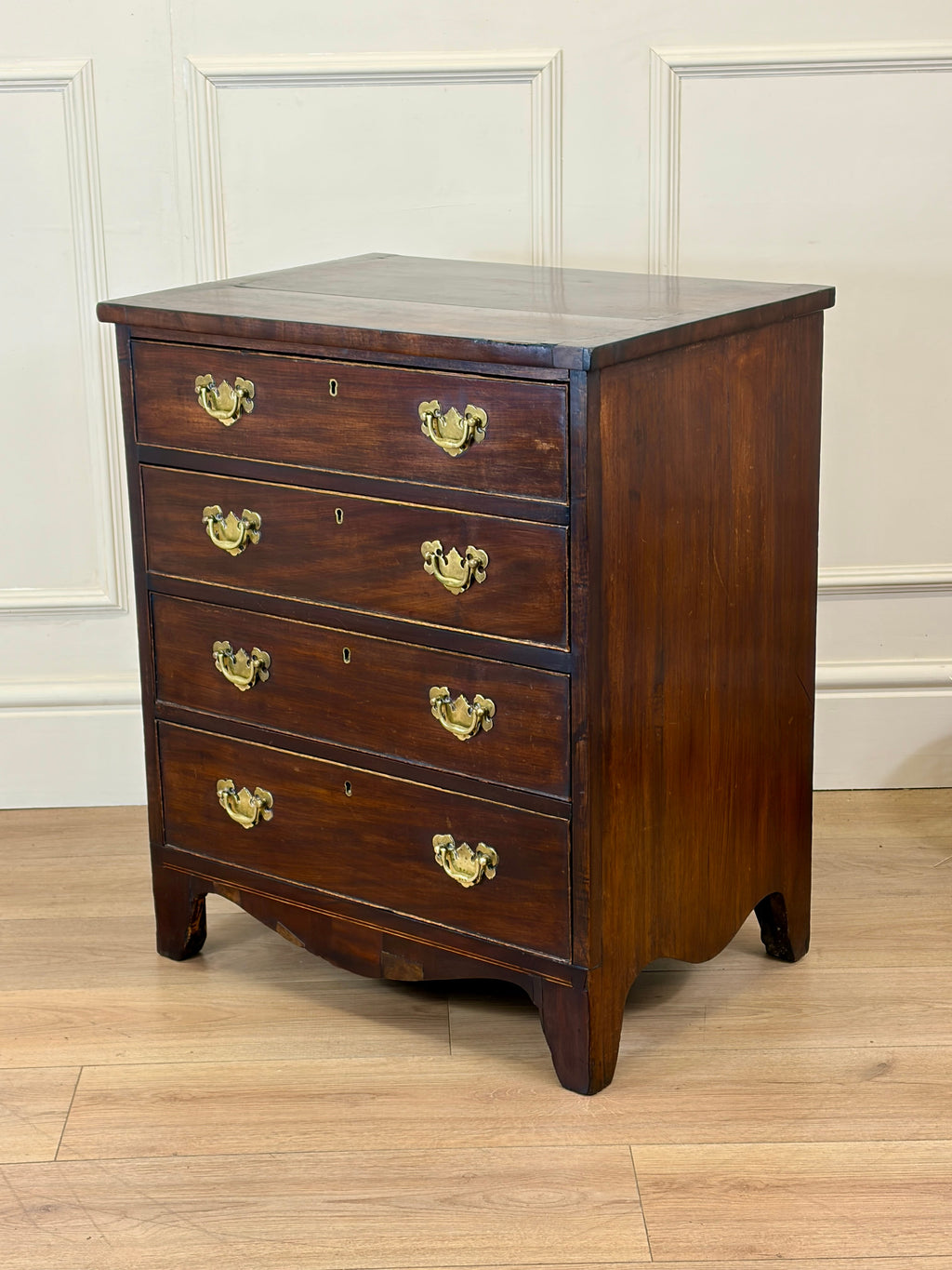 Wooden dresser with four drawers and brass handles on a wooden floor.