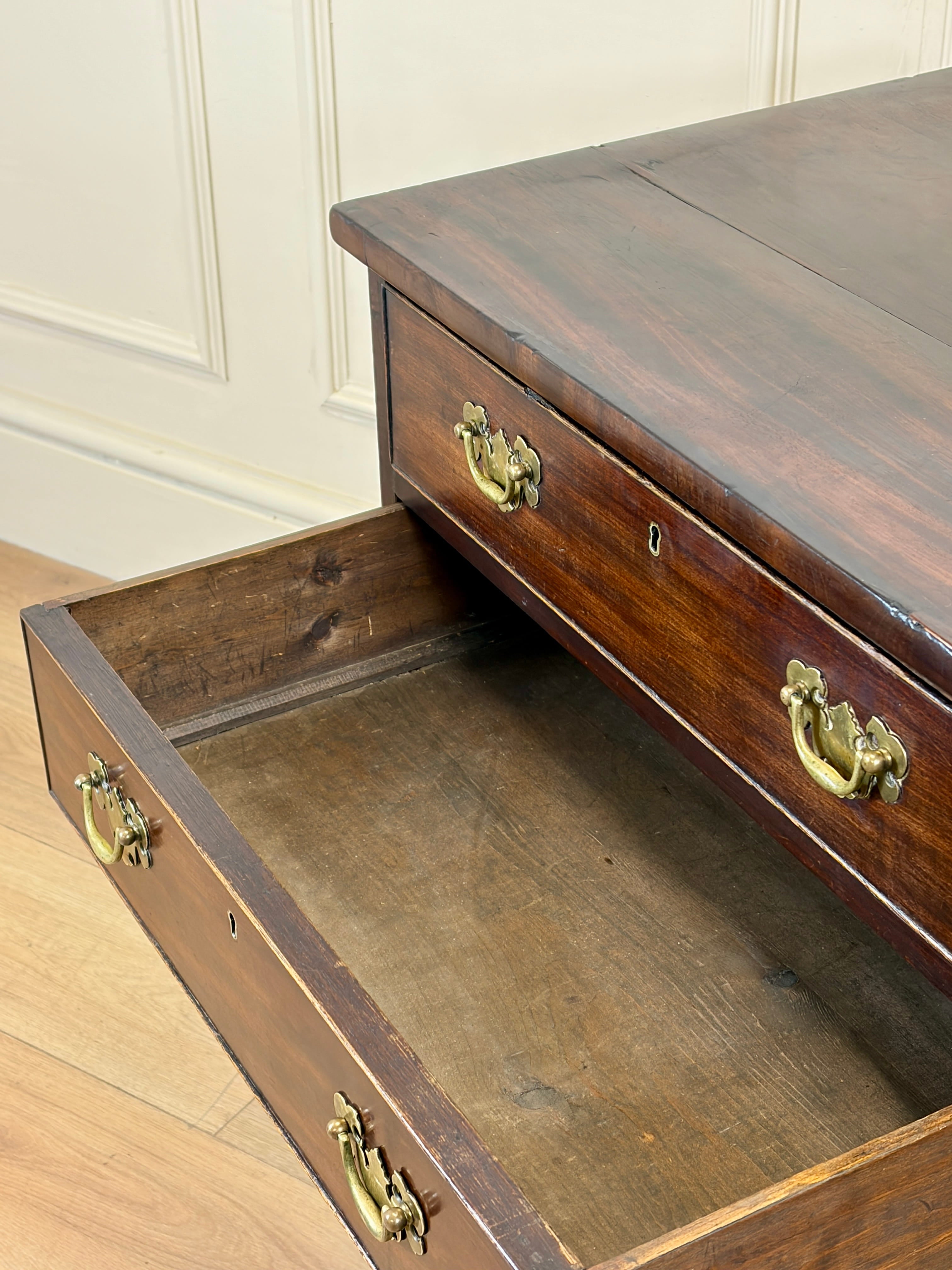 Wooden desk with an open drawer, showing brass handles, against a white paneled wall.