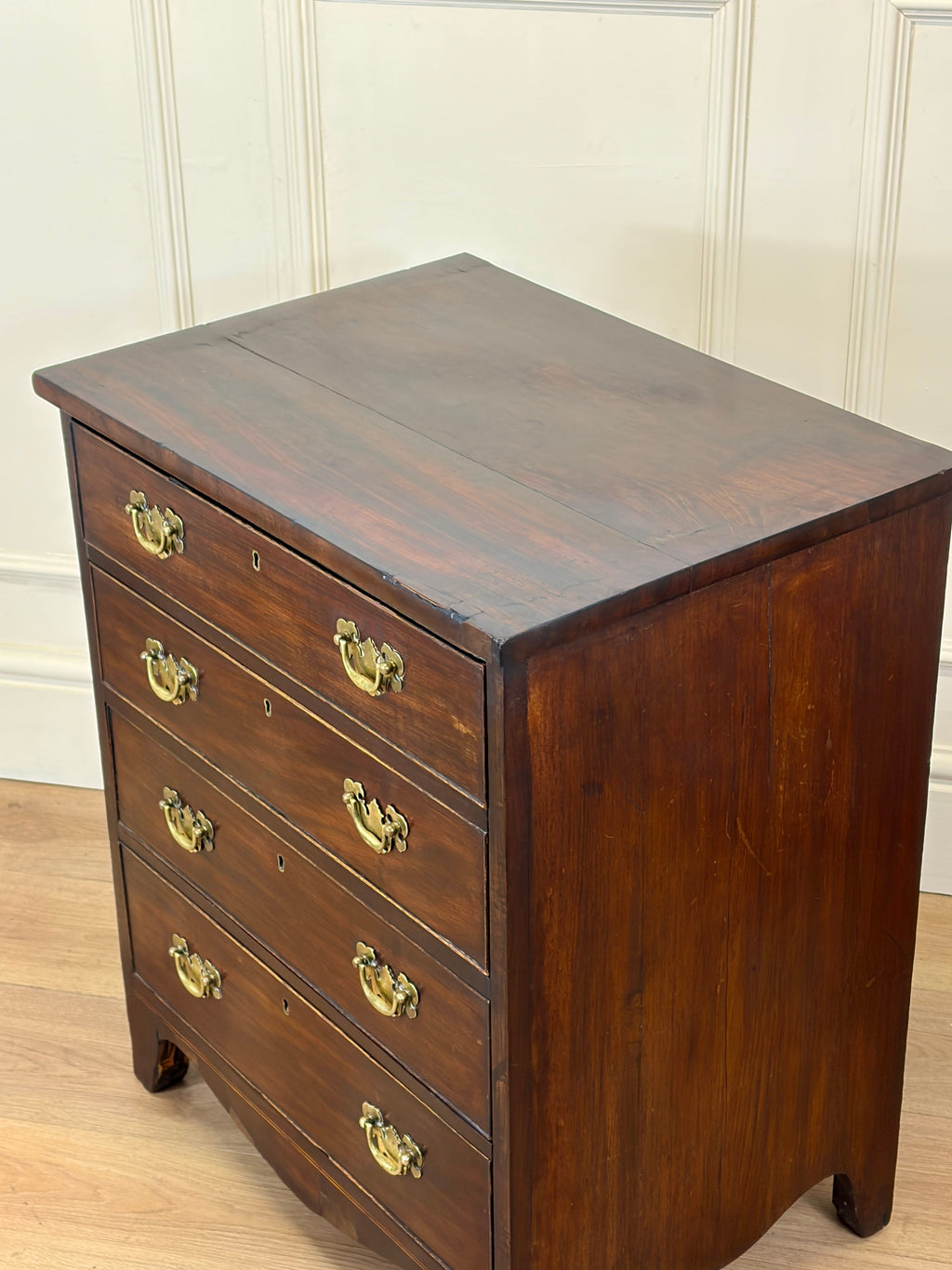 Wooden dresser with four drawers and brass handles on a wooden floor.