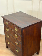 Wooden dresser with four drawers and brass handles on a wooden floor.