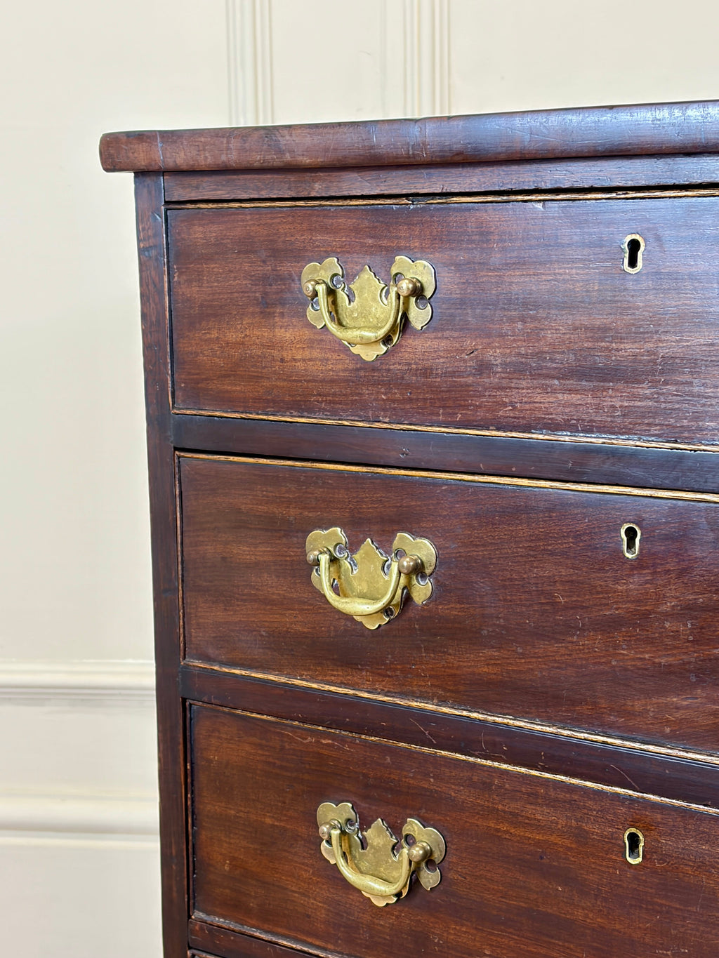 Wooden dresser with brass handles against a beige wall