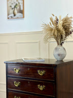 Wooden dresser with a vase of dried plants and a tablet on top, against a light wall.