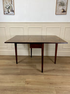 Wooden dining table with a dark finish on a wooden floor with white walls.