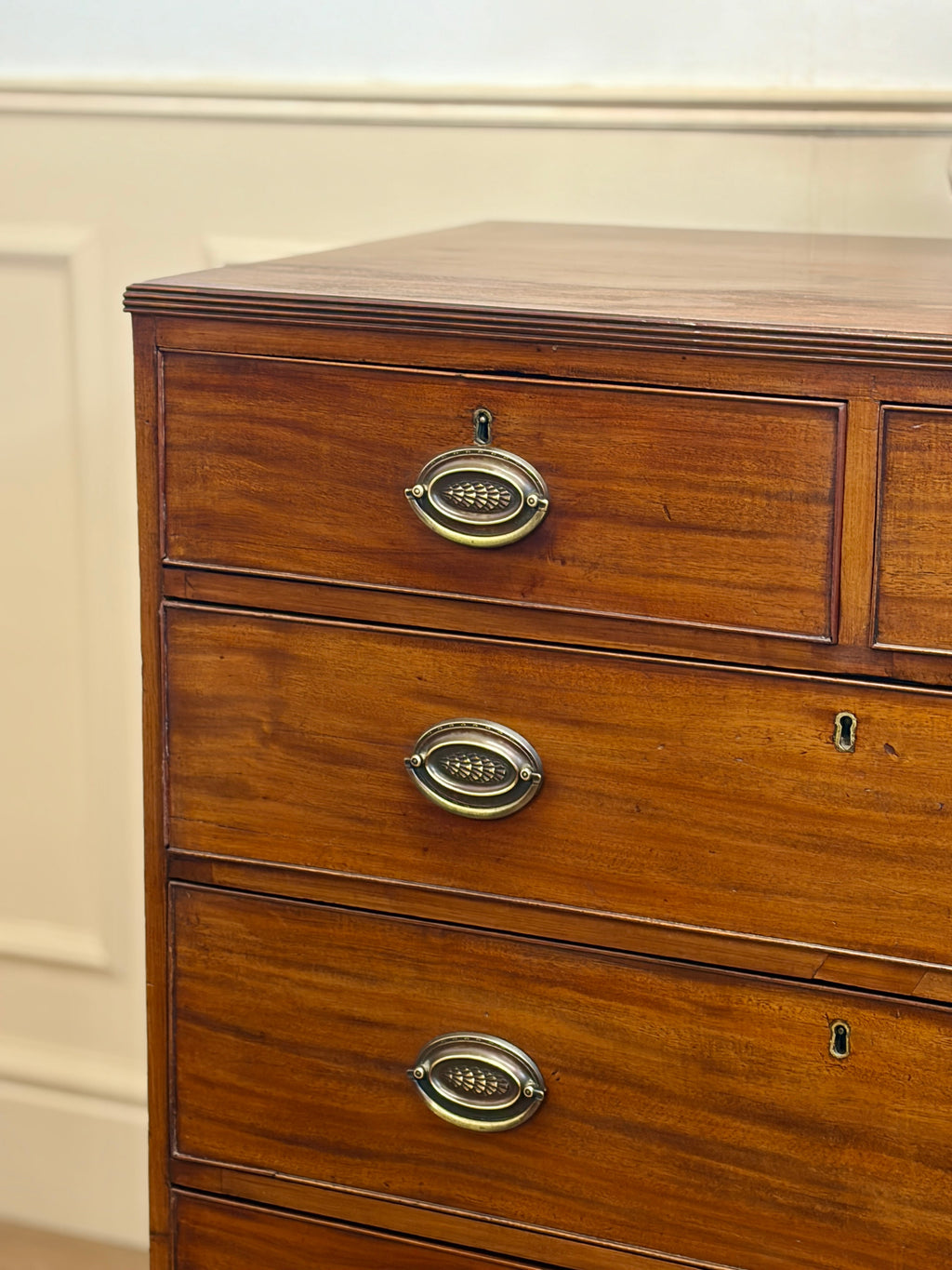 Wooden dresser with brass handles on a beige wall background