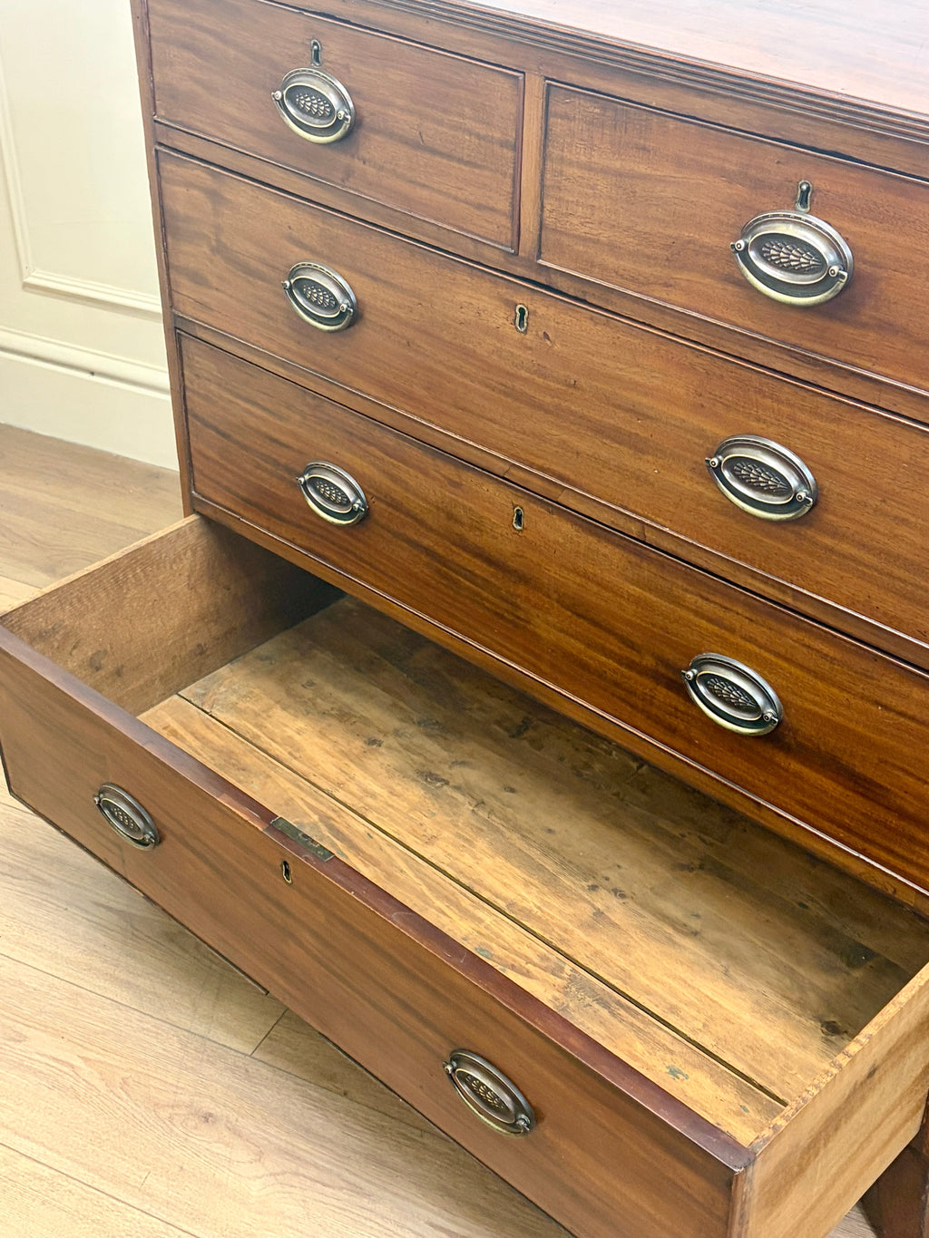 Wooden dresser with open drawer on a light wood floor.