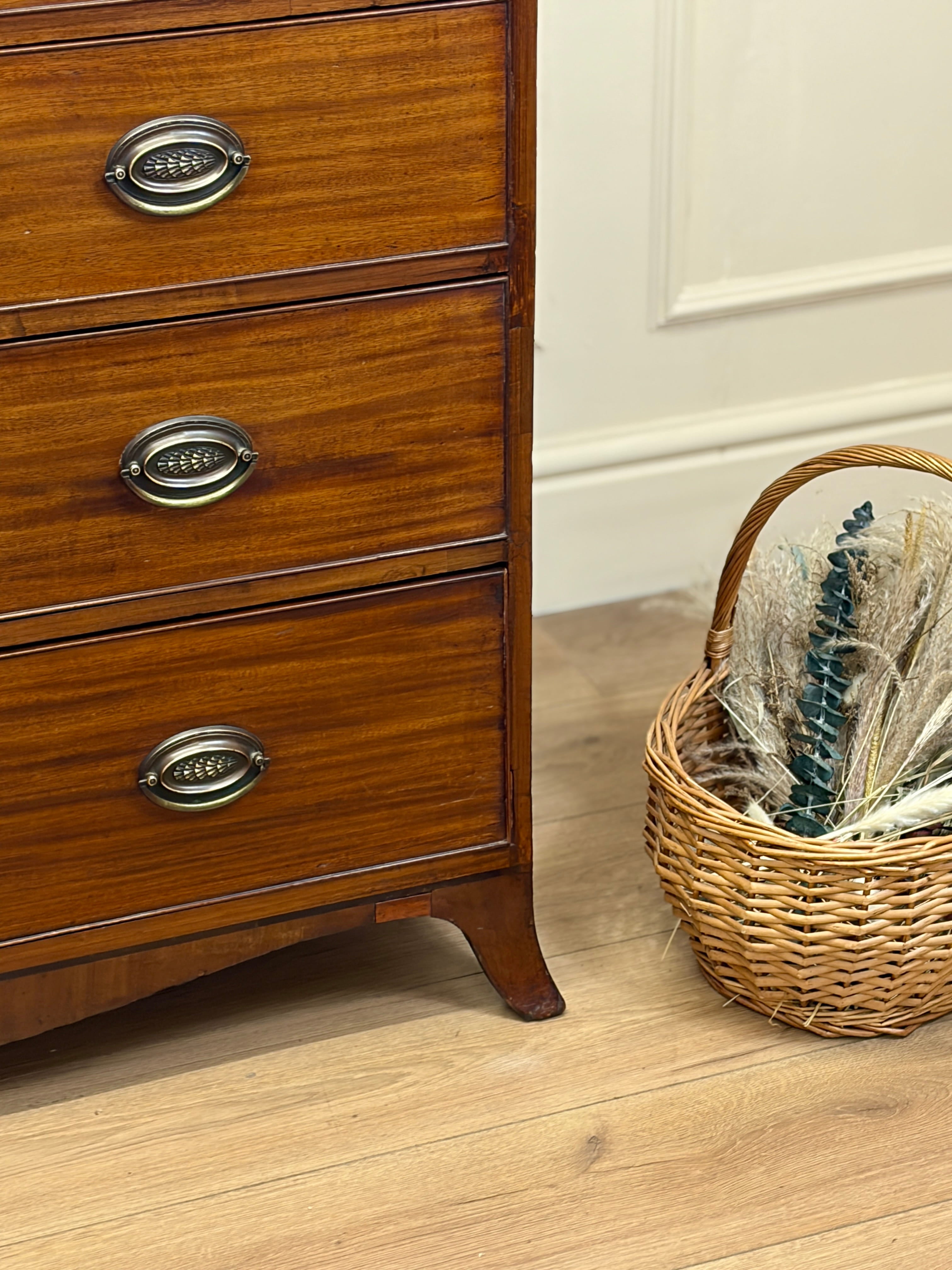Wooden dresser with metal handles on a wooden floor next to a wicker basket.