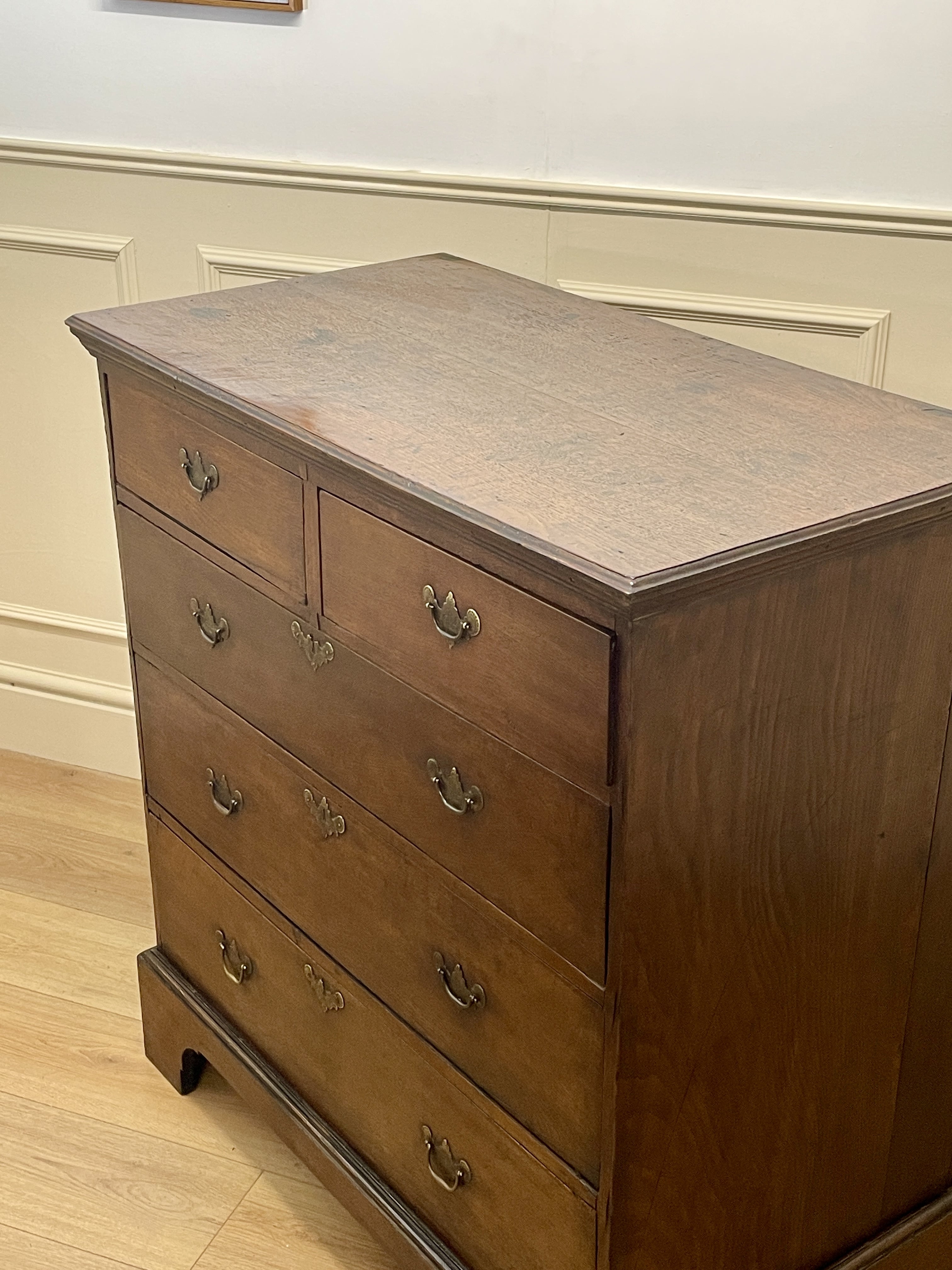 Mid-18th century antique Georgian oak chest of drawers with caddy moulded top, two short and three long graduated drawers, original brass handles, and bracket feet.