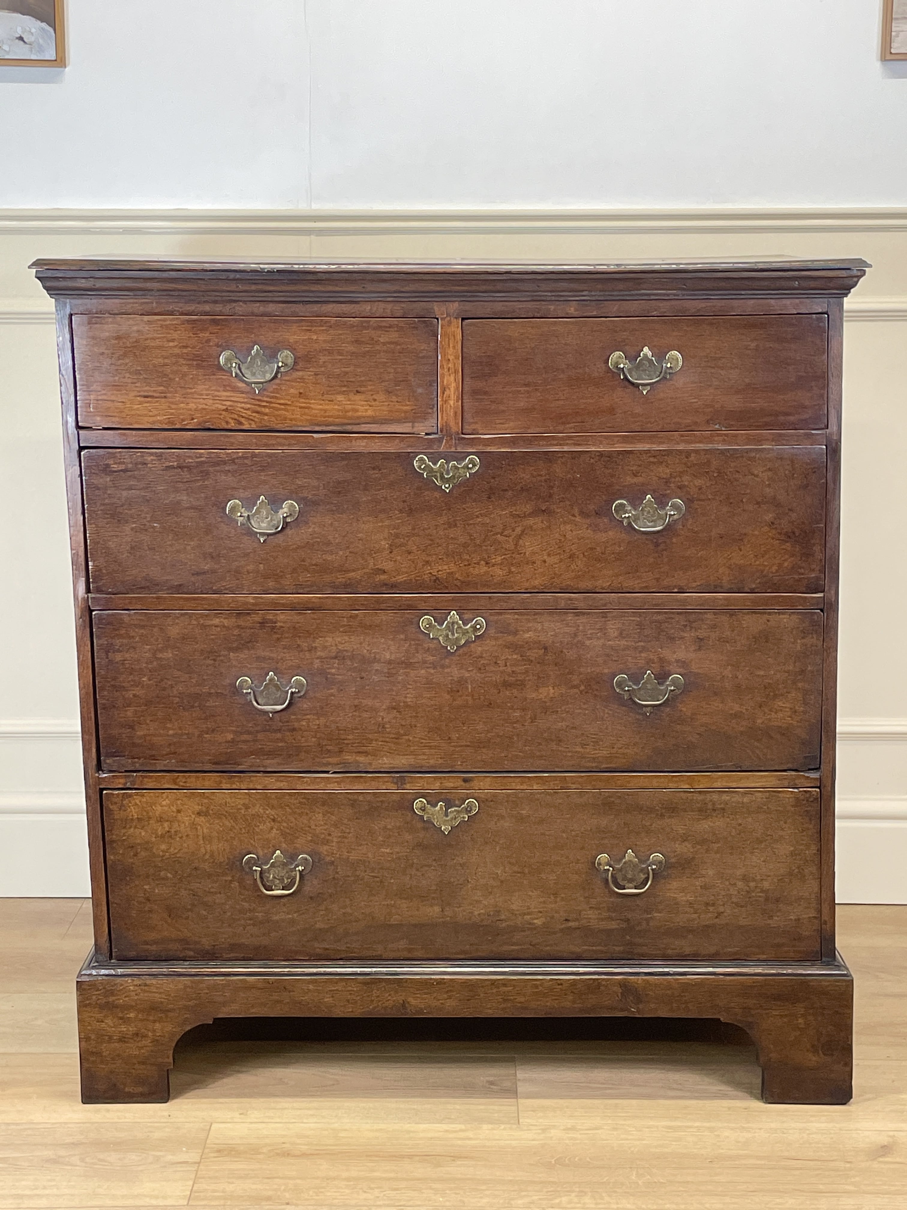 Mid-18th century antique Georgian oak chest of drawers with caddy moulded top, two short and three long graduated drawers, original brass handles, and bracket feet.