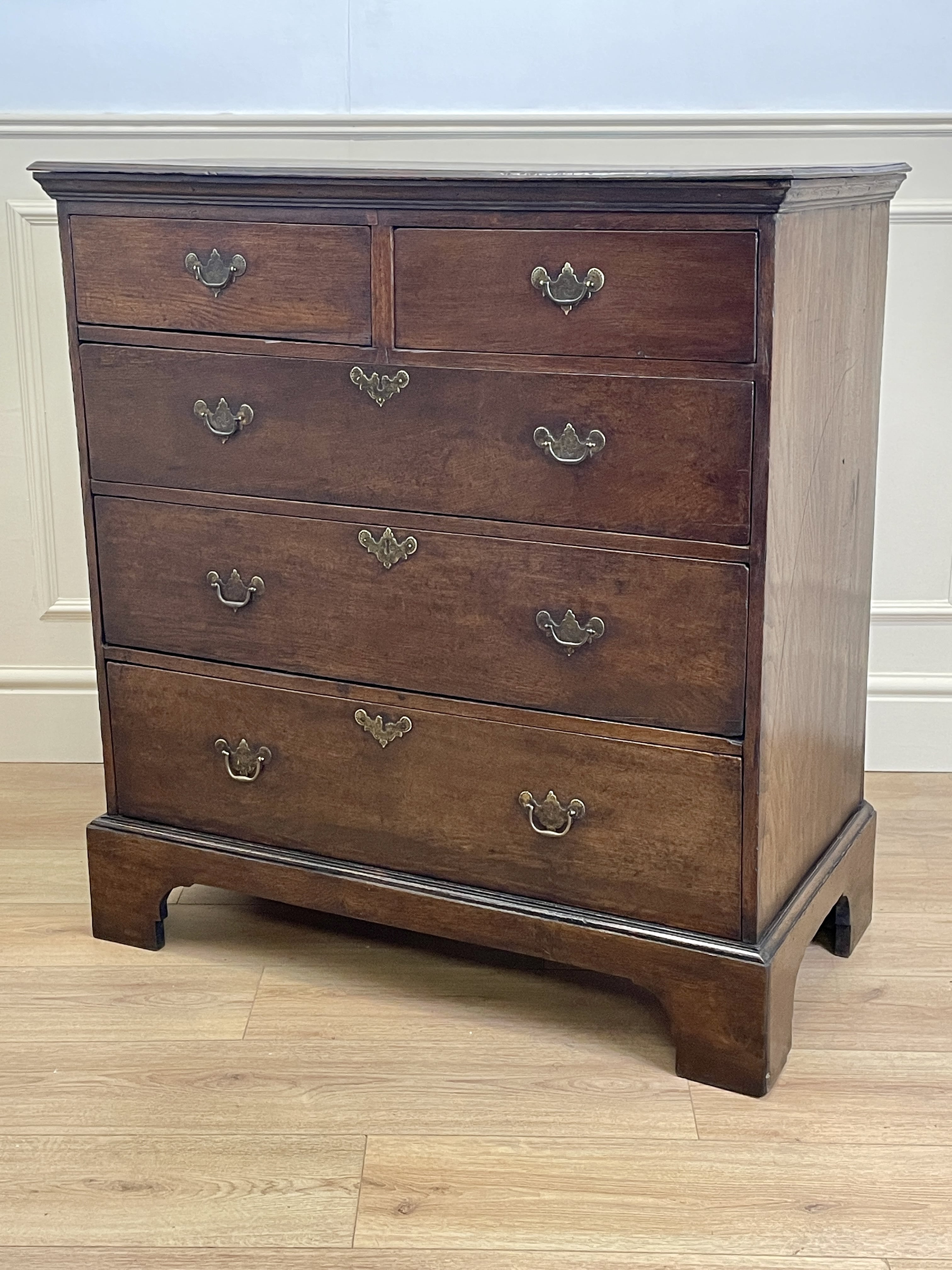 Mid-18th century antique Georgian oak chest of drawers with caddy moulded top, two short and three long graduated drawers, original brass handles, and bracket feet.