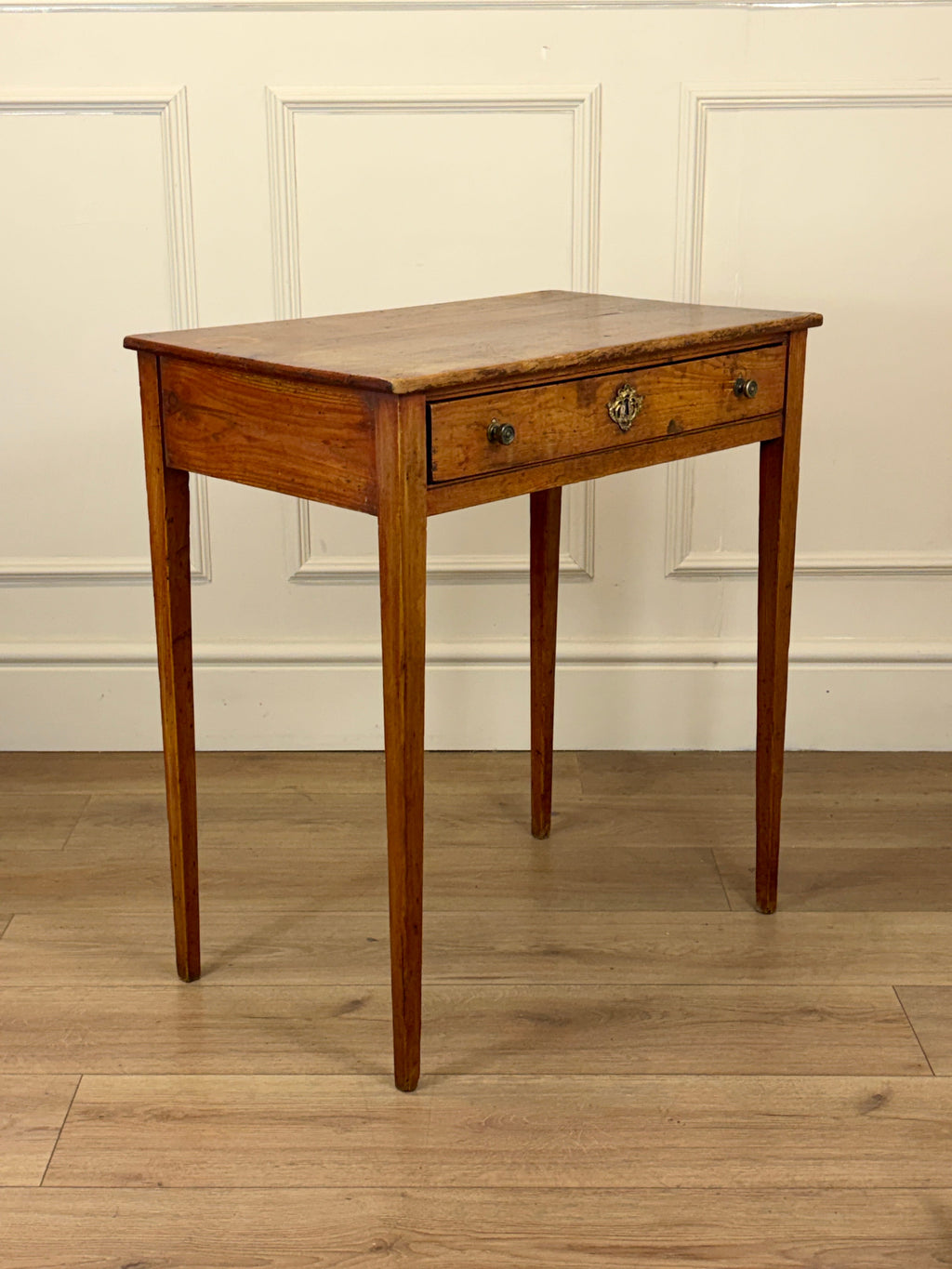 Wooden side table with a single drawer against a white paneled wall.