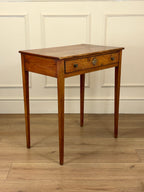 Wooden side table with a single drawer against a white paneled wall.