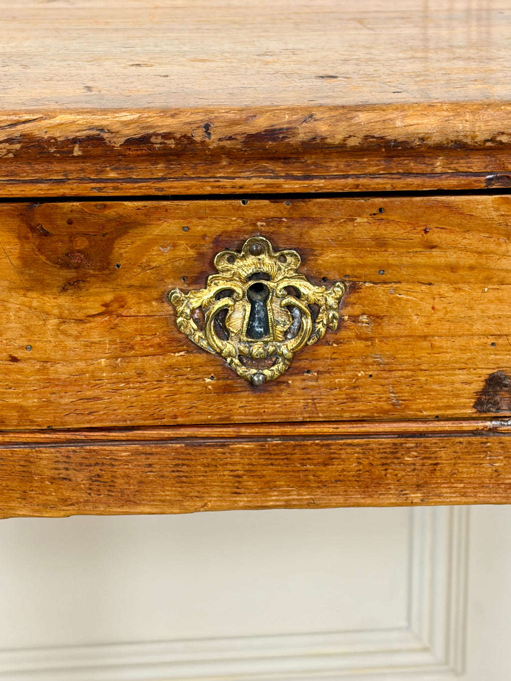 Wooden drawer with a decorative brass lock on a white wall.