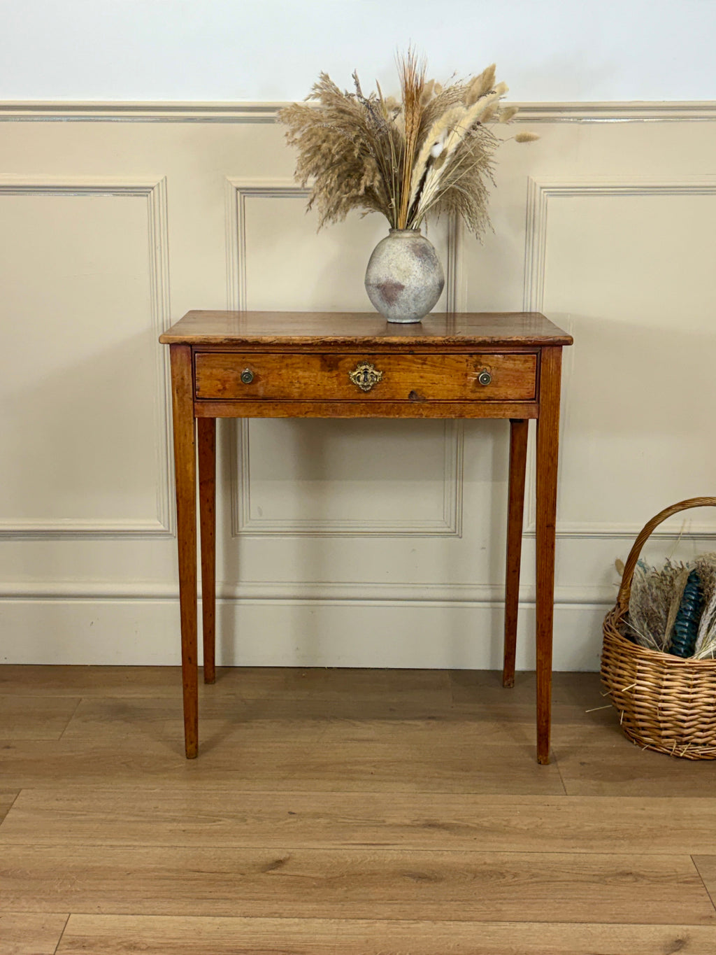 Wooden side table with a vase of dried plants against a neutral wall.