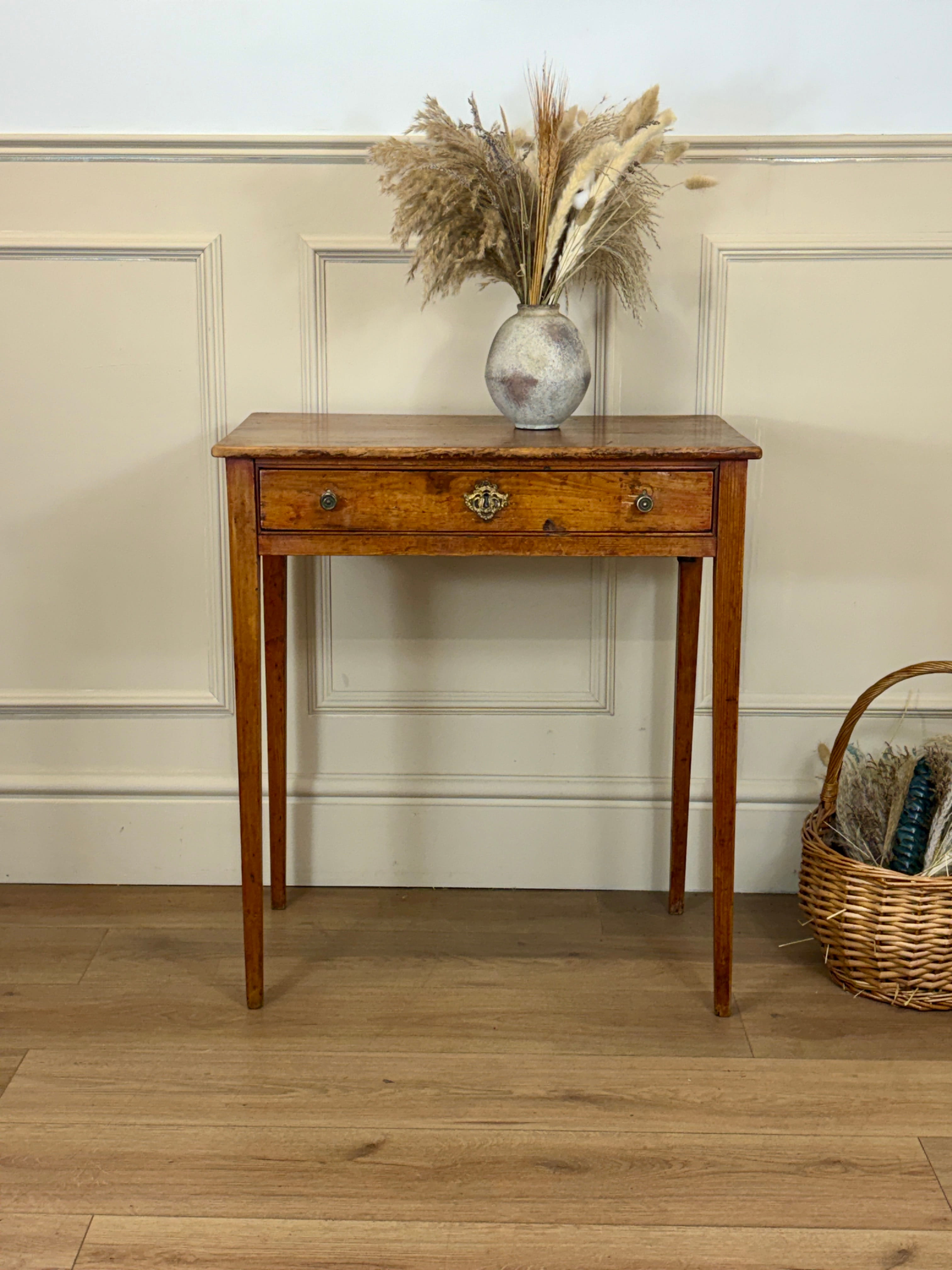 Wooden side table with a vase of dried plants against a neutral wall.