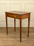 Wooden side table with a single drawer against a white paneled wall.