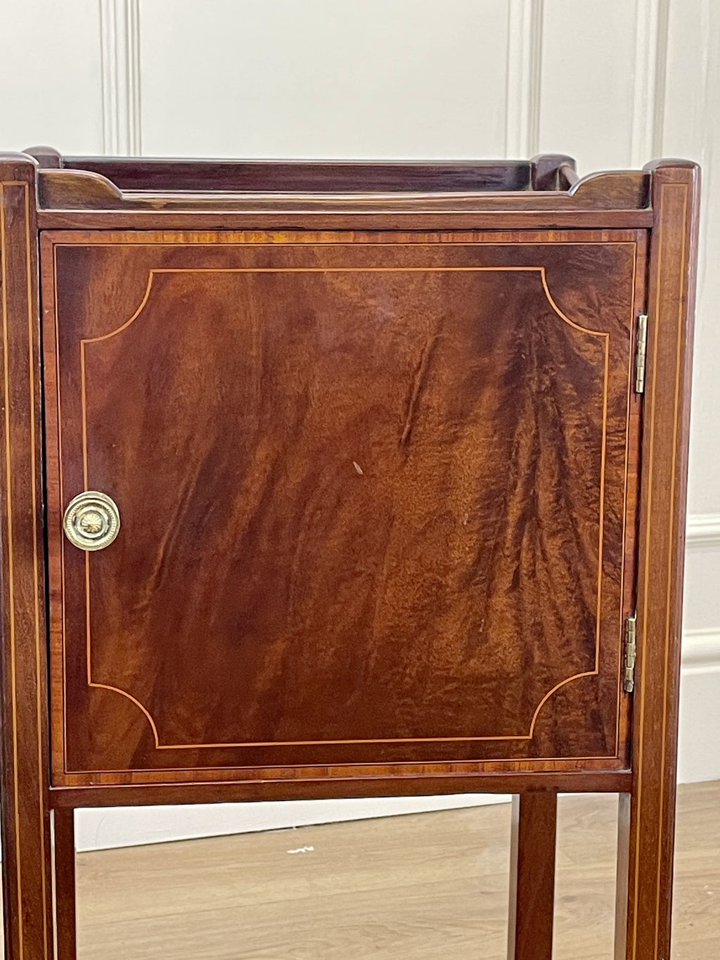 Wooden side table with a door and brass handle on a wooden floor.