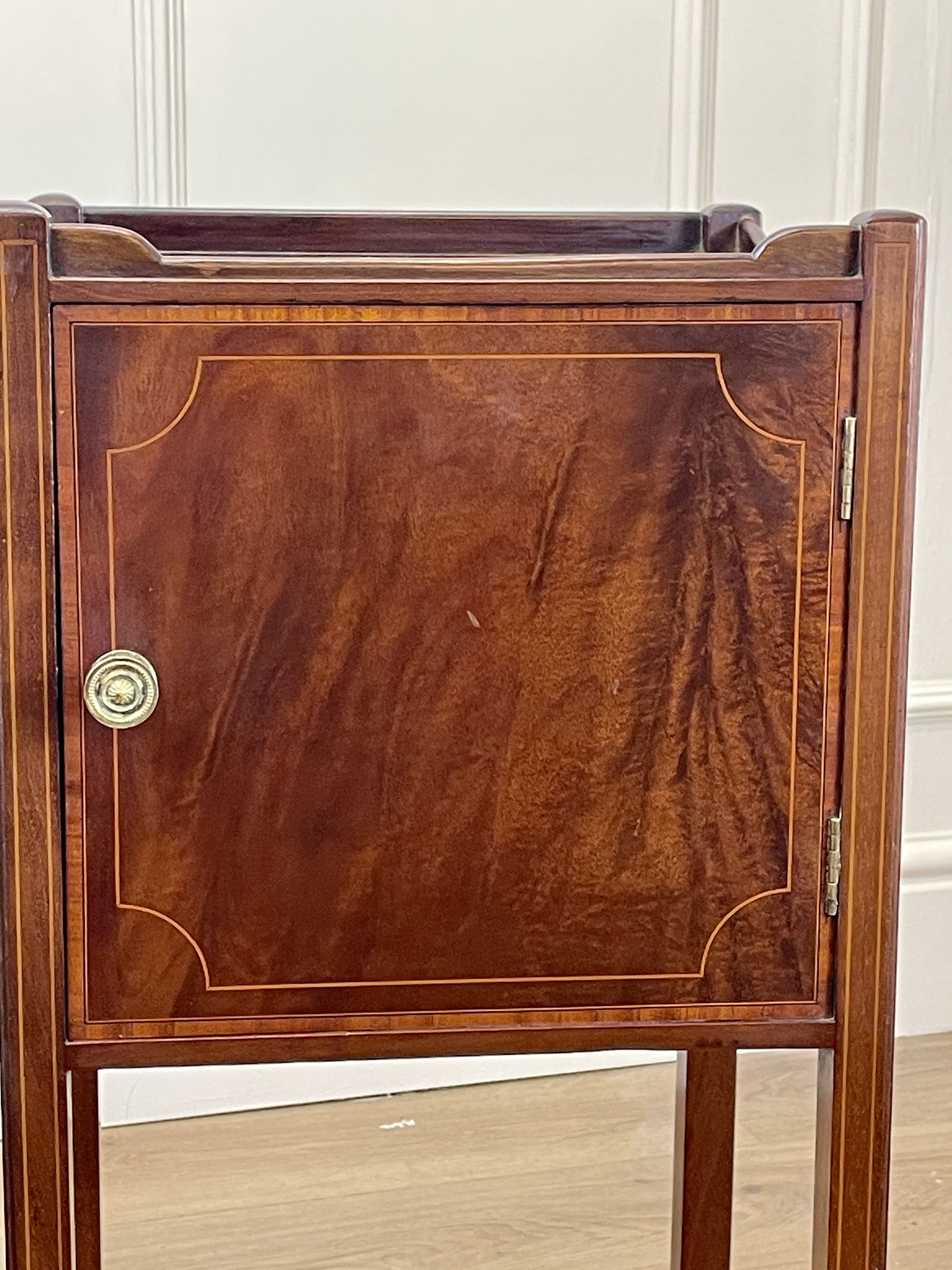 Wooden side table with a door and brass handle on a wooden floor.