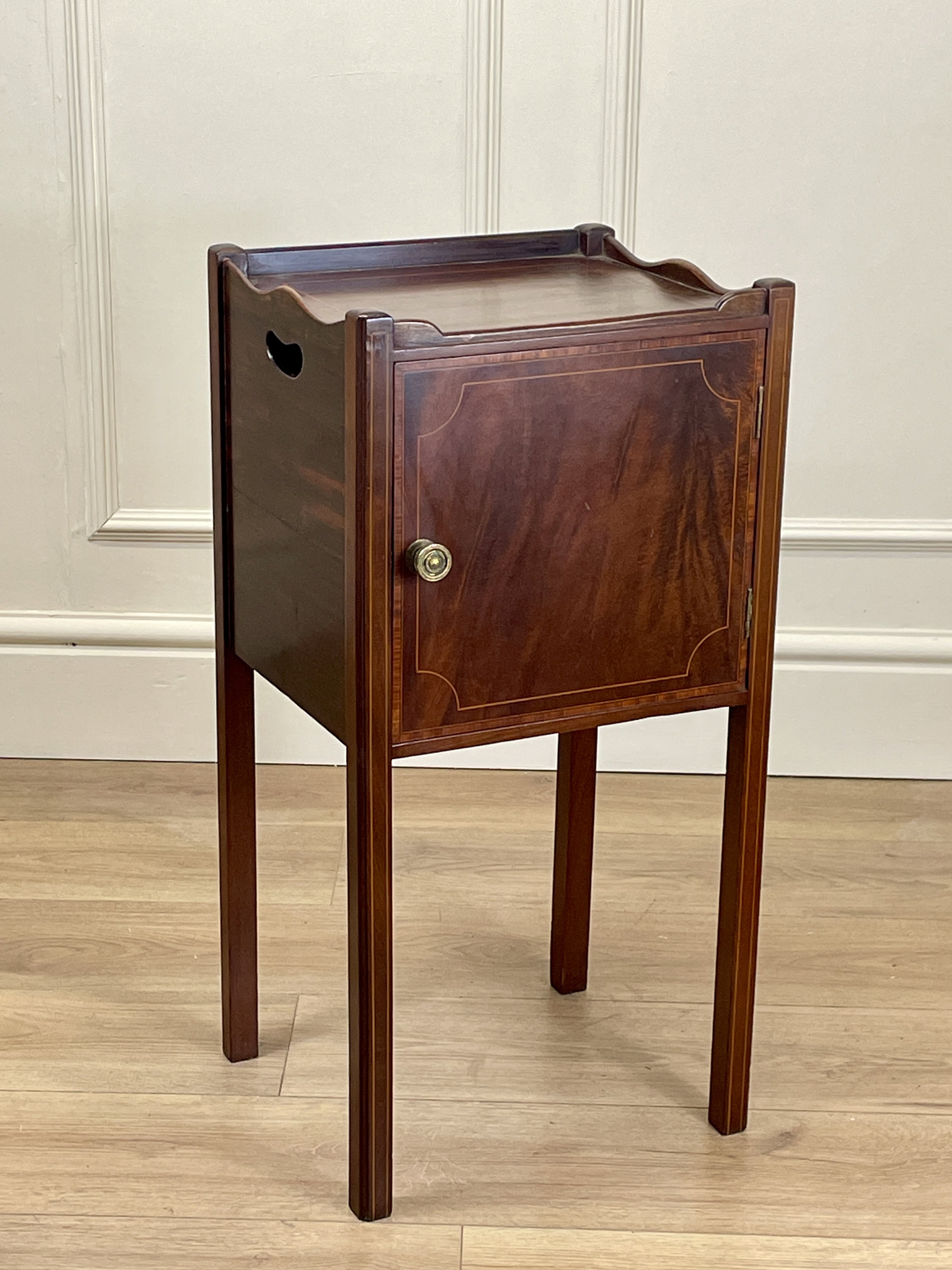 Wooden side table with a cabinet door on a wooden floor against a white paneled wall.