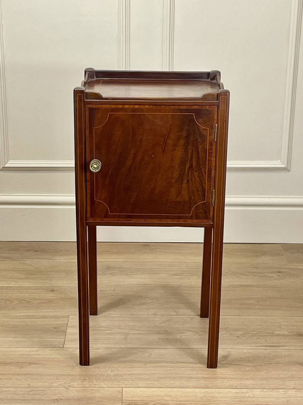 Wooden side table with a cabinet against a white paneled wall.