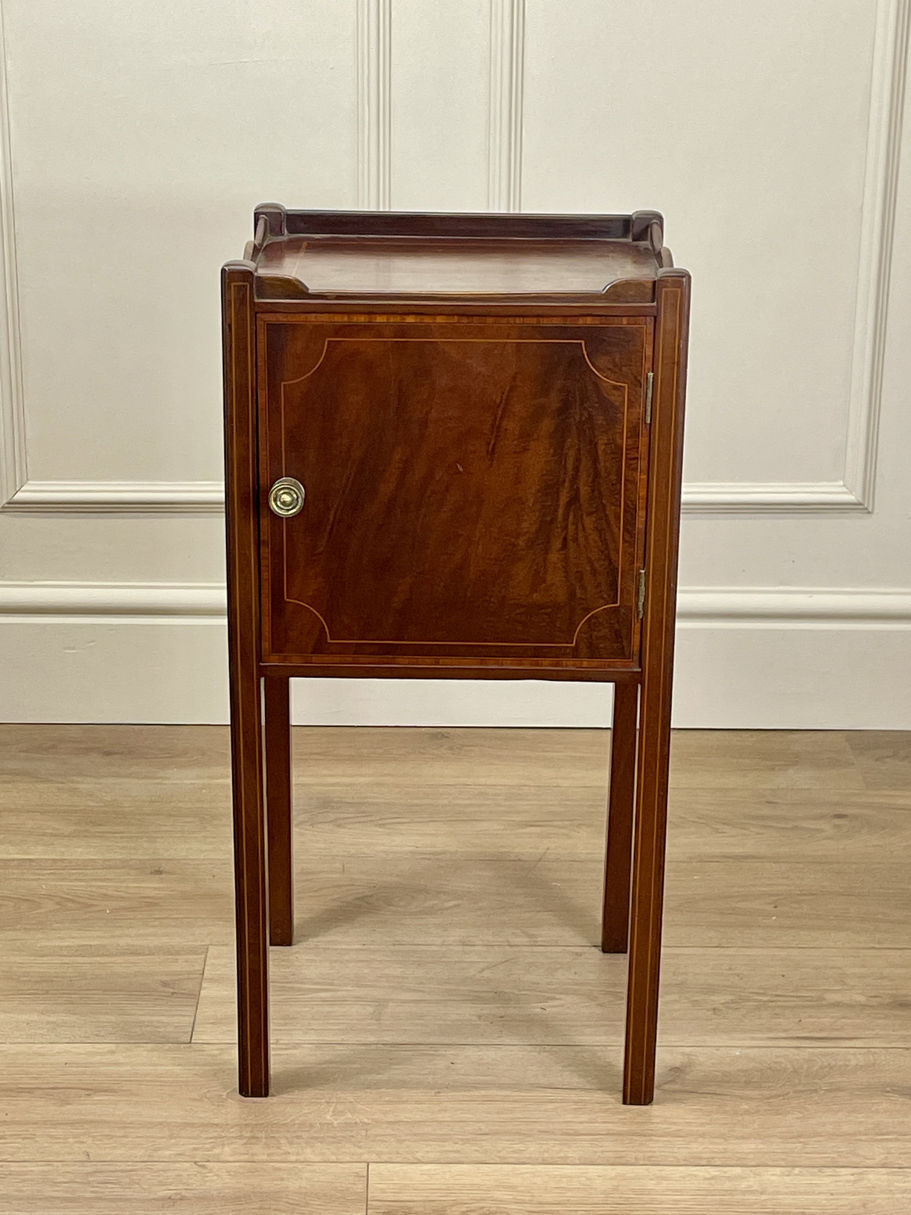 Wooden side table with a cabinet against a white paneled wall.