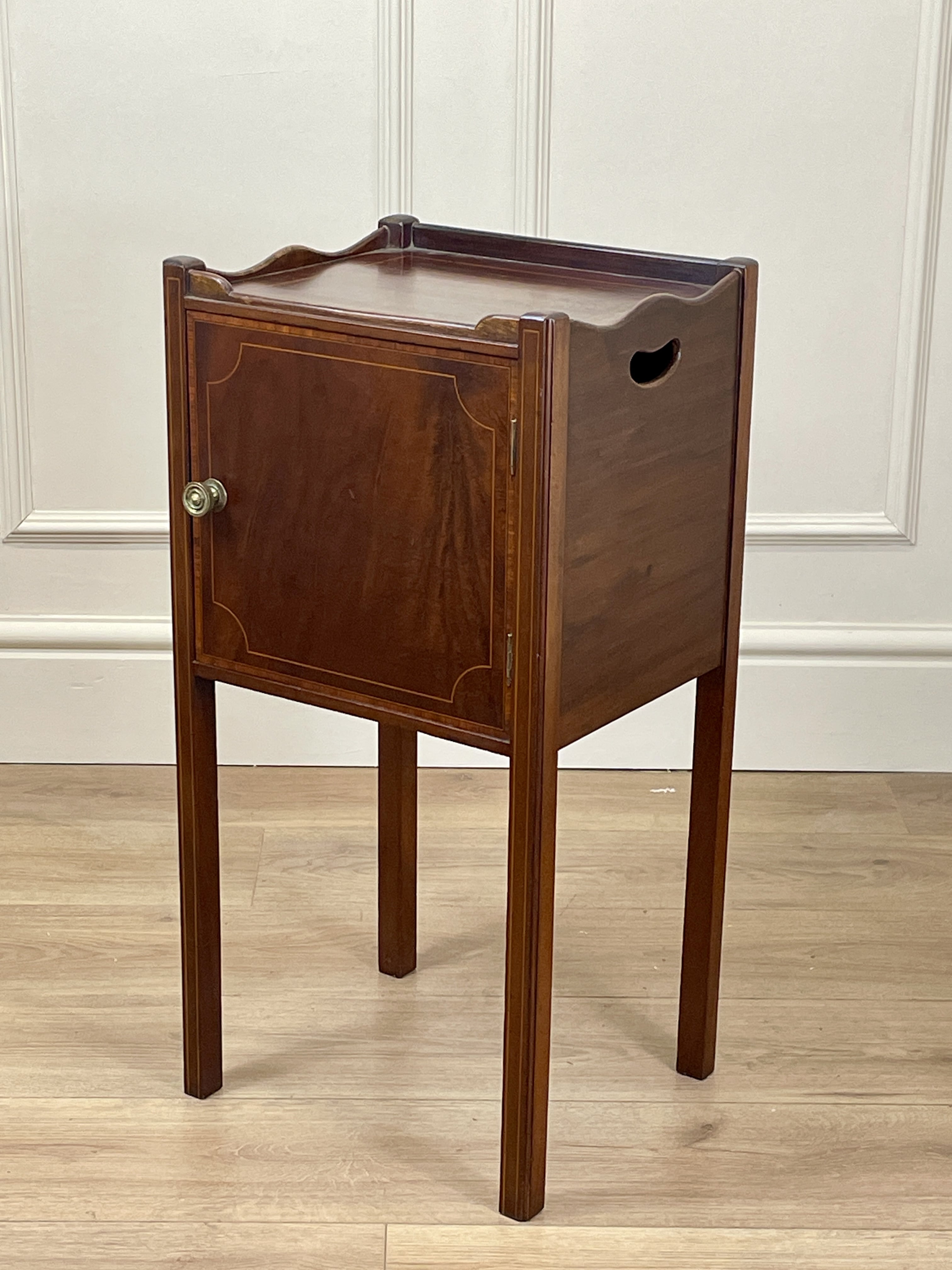 Wooden side table with a tray on top against a white wall.