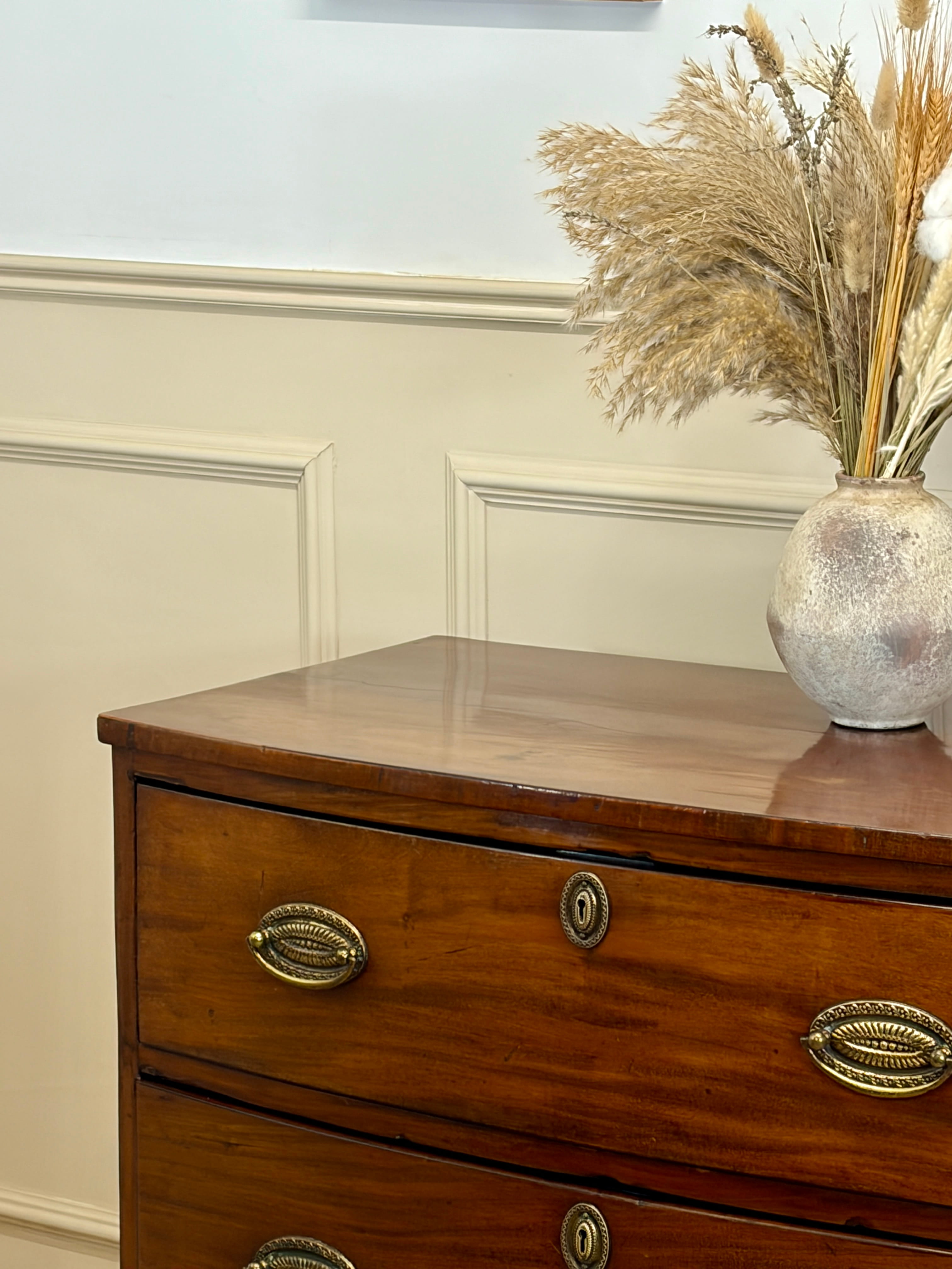 Wooden dresser with decorative vase and pampas grass against a beige wall.