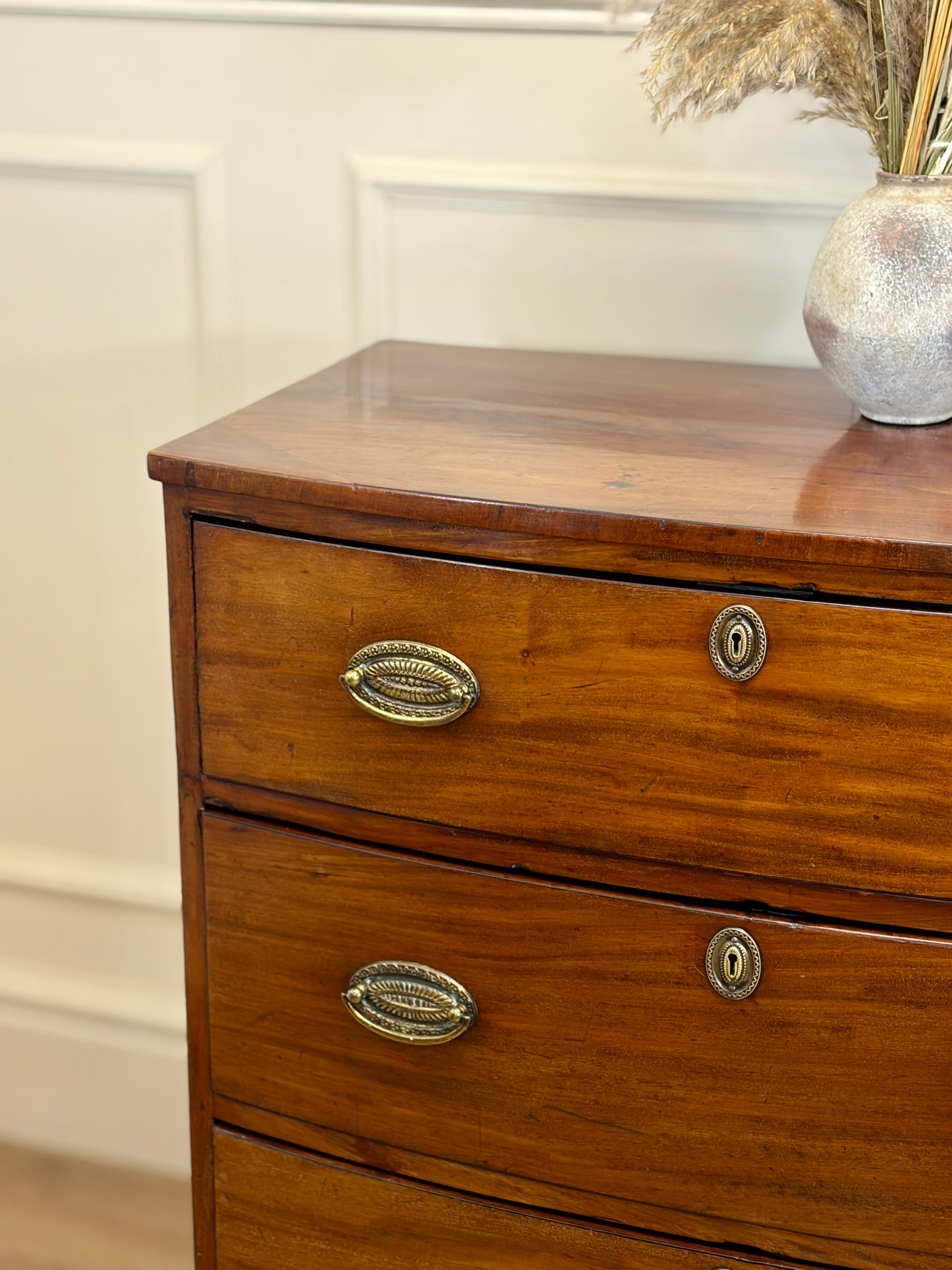 Wooden dresser with brass handles and a vase on top against a neutral wall.