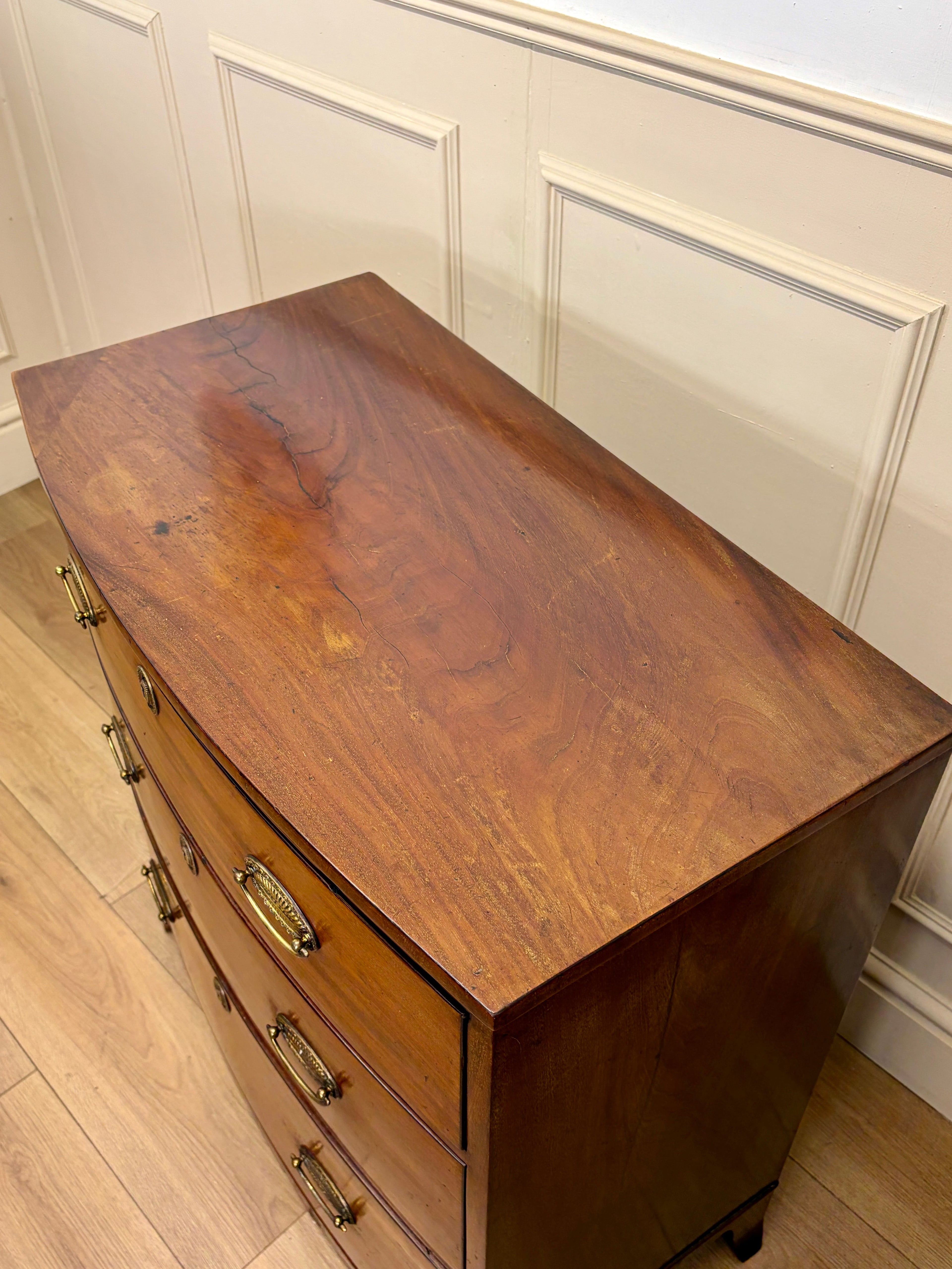 Wooden dresser with brass handles against a white paneled wall.