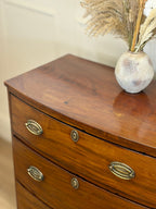 Wooden dresser with brass handles and a vase with dried plants on top.
