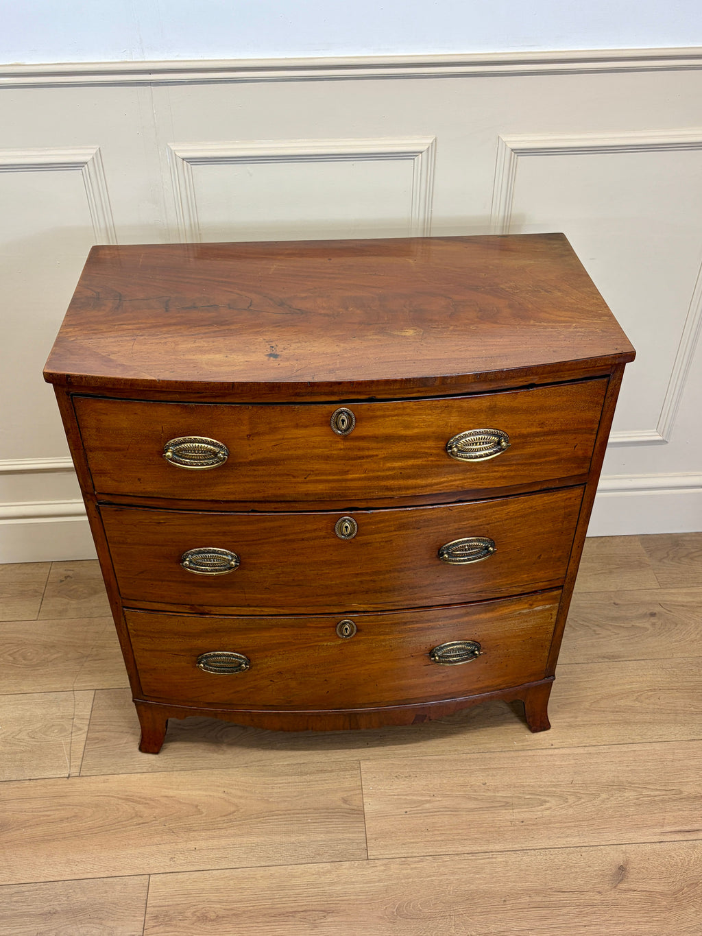 Wooden dresser with three drawers on a wooden floor against a white paneled wall.